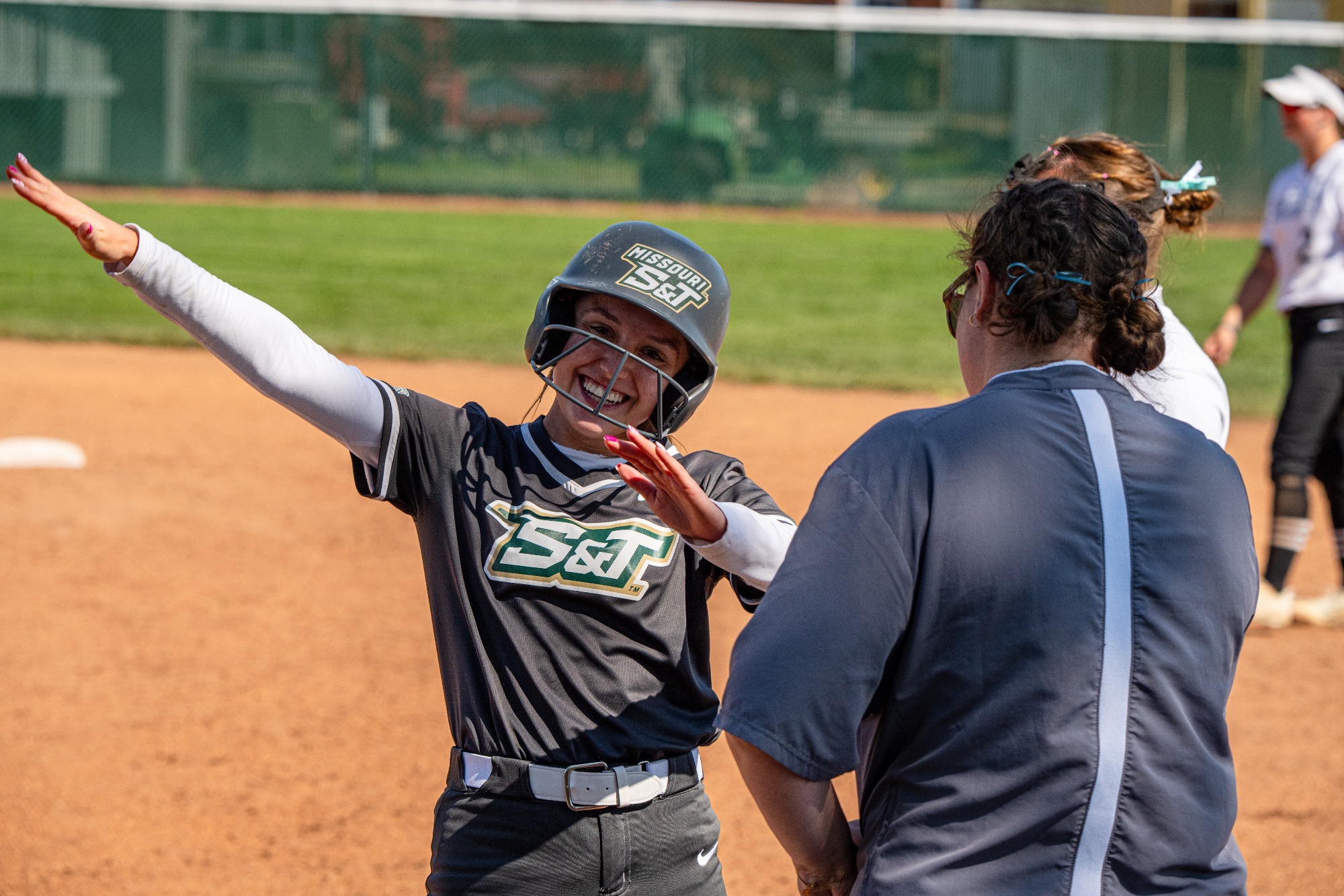 Joselyn Ulloa of Missouri S&T softball celebrates at home plate, smiling and raising her arms as she greets her coach following a scoring play.