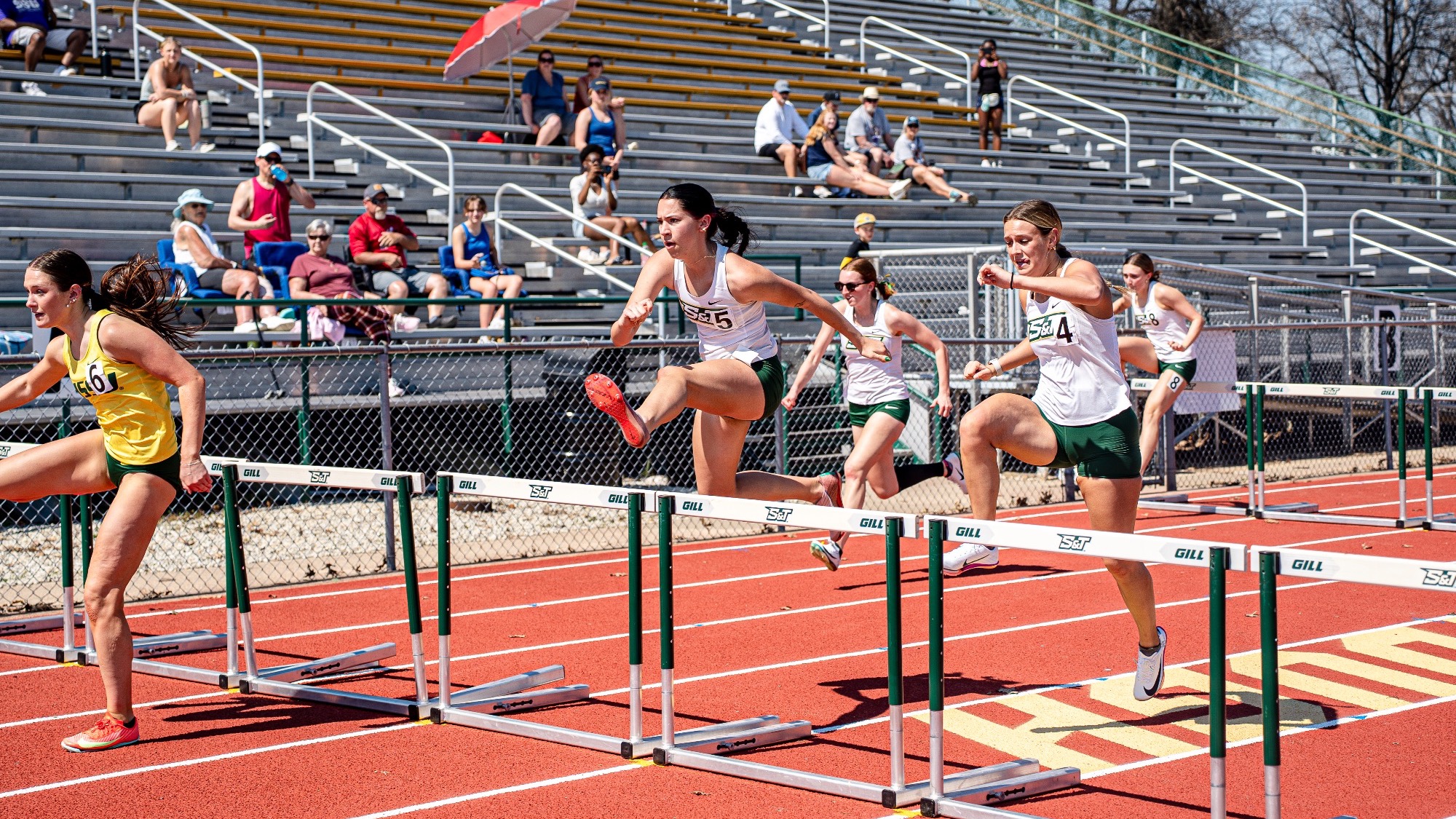 Missouri S&T hurdlers Lauryn Fenoglio and Alexis Lay clear hurdles side by side during the 100-meter hurdles at the Miner Invitational at Allgood-Bailey Stadium, competing alongside runners from other teams.