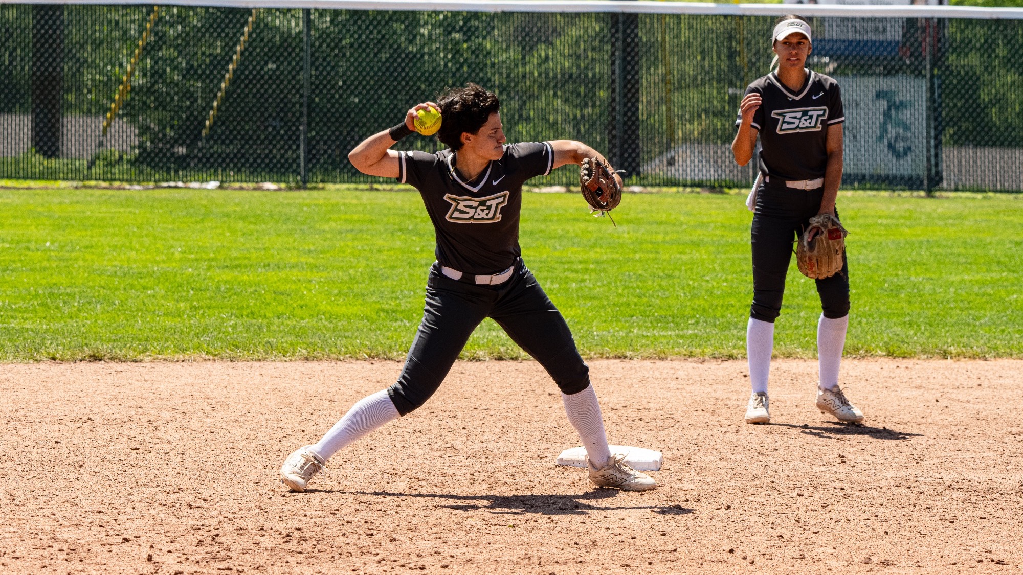 Missouri S&T softball player Taylor Nelson getting ready to launch a ball at shortstop to first baseman during a game against Quincy at the Missouri S&T softball field. Second baseman Claire Lopez is in the background watching Nelson as they are both wearing grey S&T softball jerseys.
