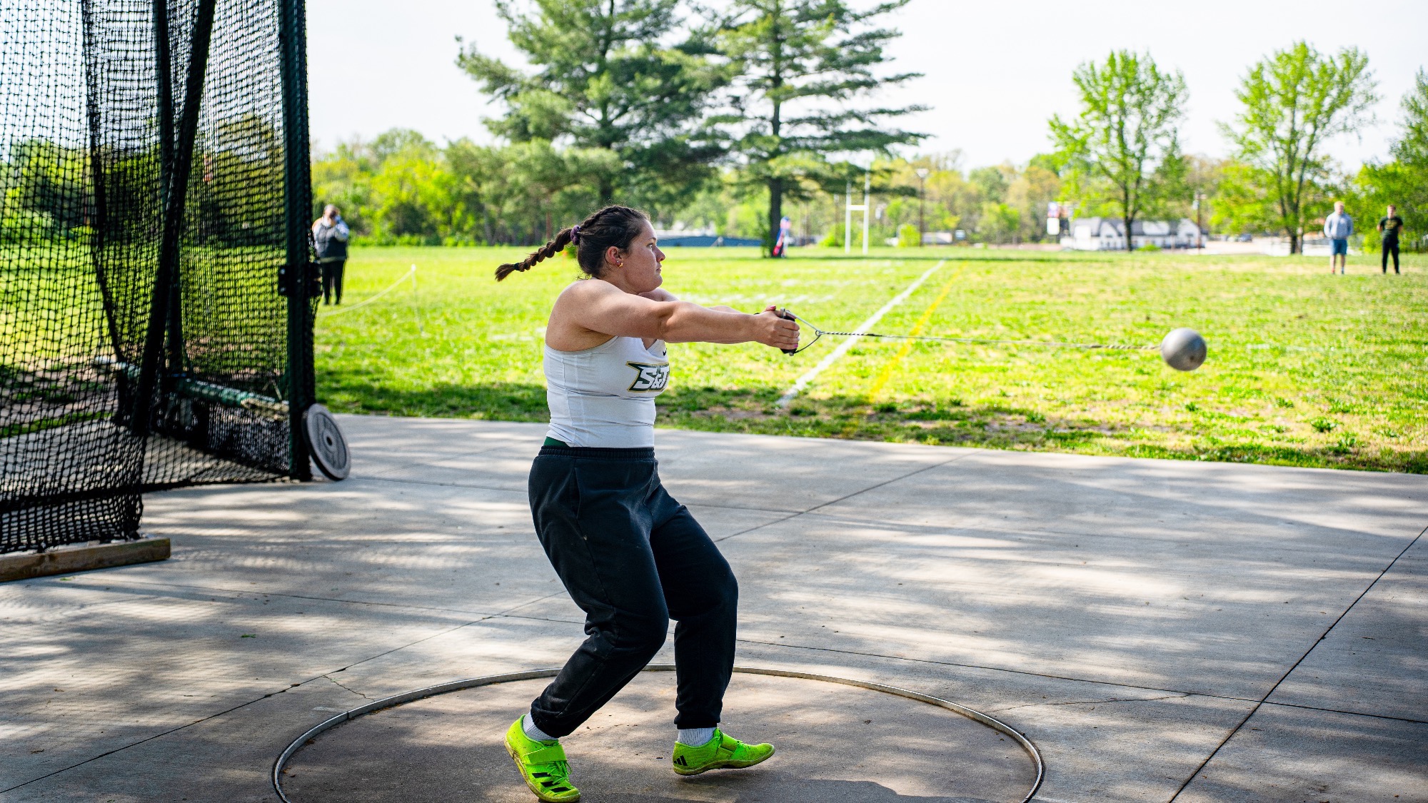 Madelaine Fischer of Missouri S&T competes in the hammer throw, spinning in the throwing circle as the hammer extends outward, with spectators and trees visible in the background.