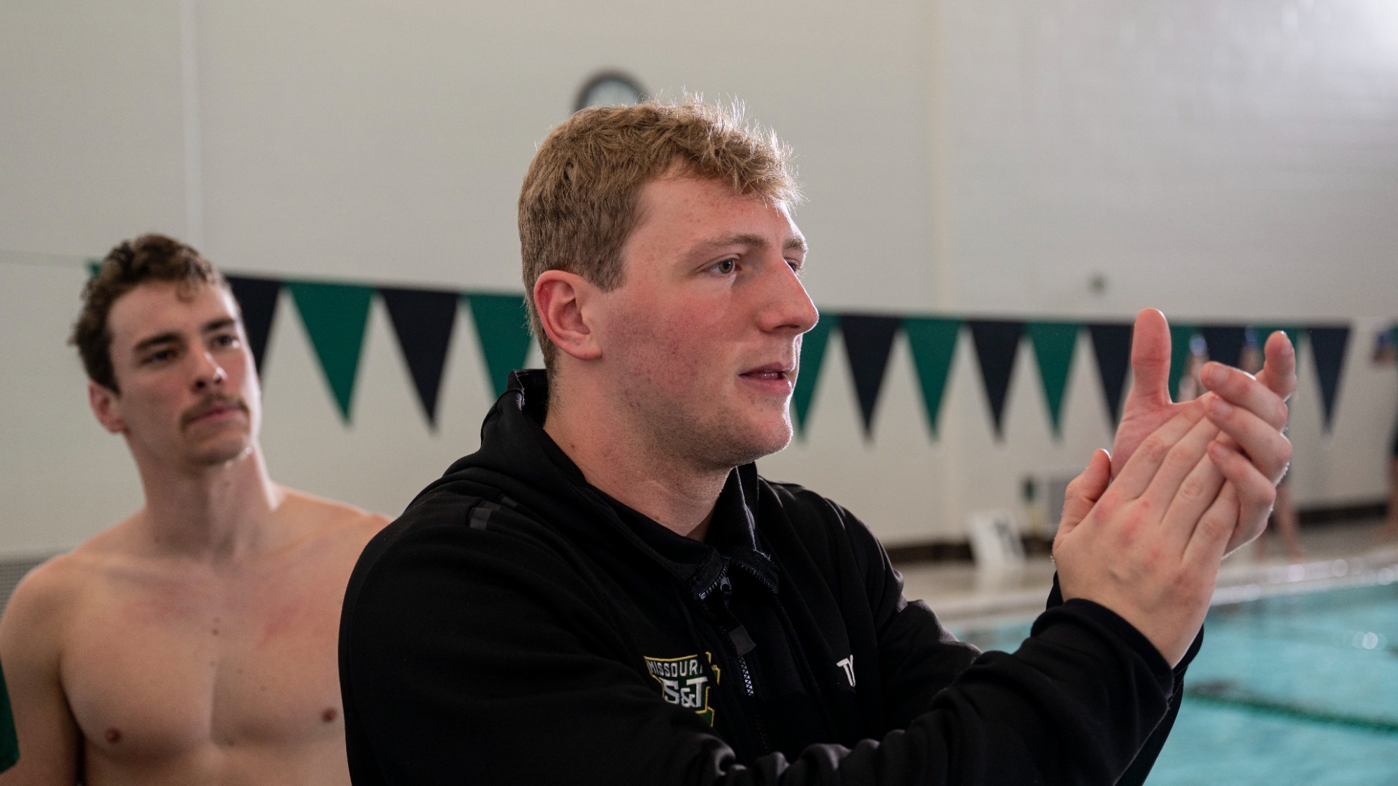 Jordan Christensen photographed standing by the S&T swimming pool and clapping. He is wearing a black hoodie.