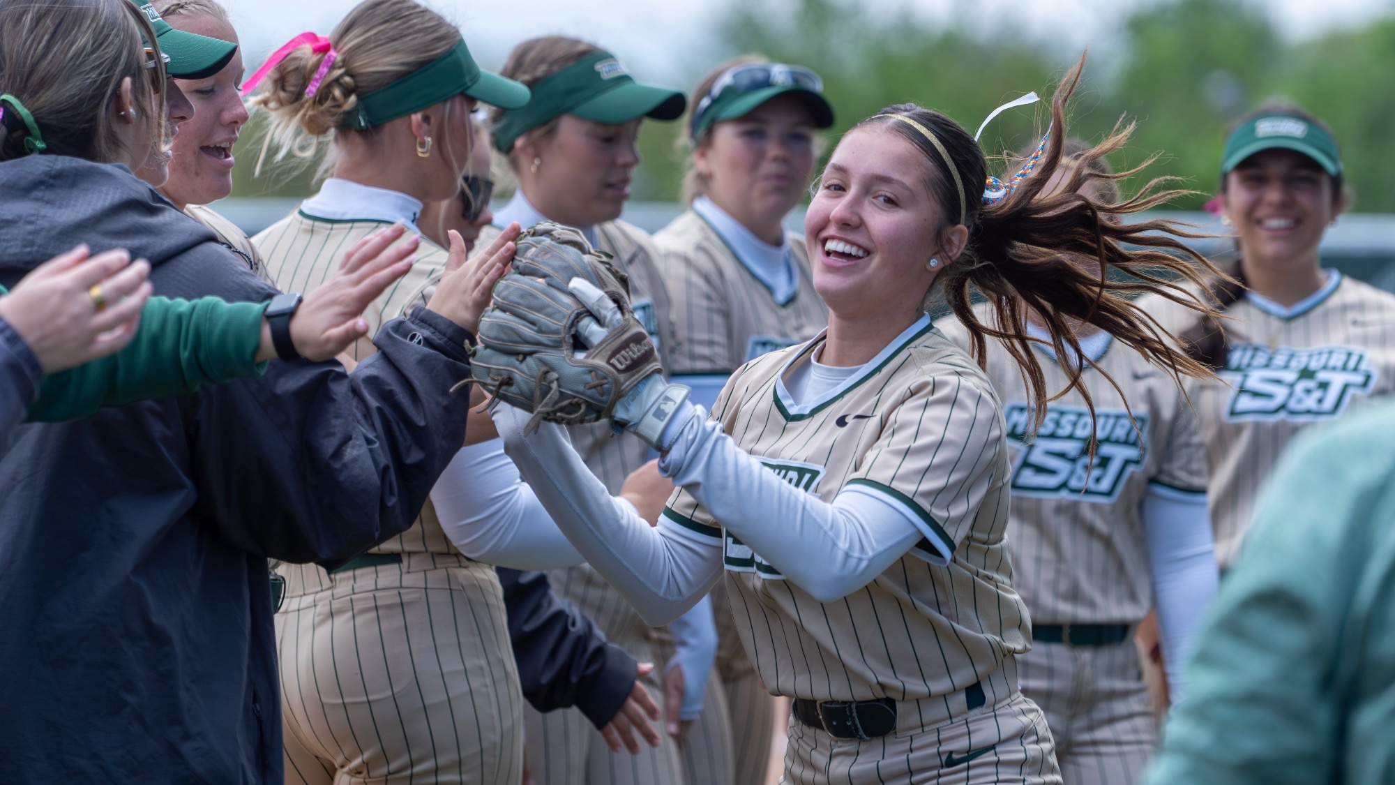 Missouri S&T Joselyn Ulloa in gold pinstripes jersey high-fiving her teammates during starting lineups at the Missouri S&T softball field.