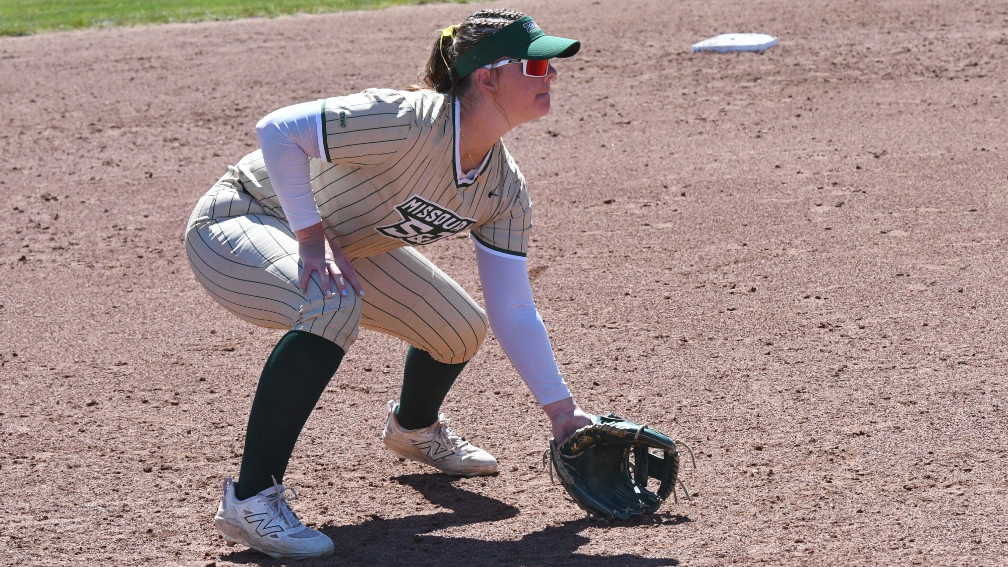 Missouri S&T third baseman Molly Fitzgerald sets in a defensive stance on the infield dirt, wearing a gold pinstripe Miners jersey and ready for a play at the Missouri S&T softball field.
