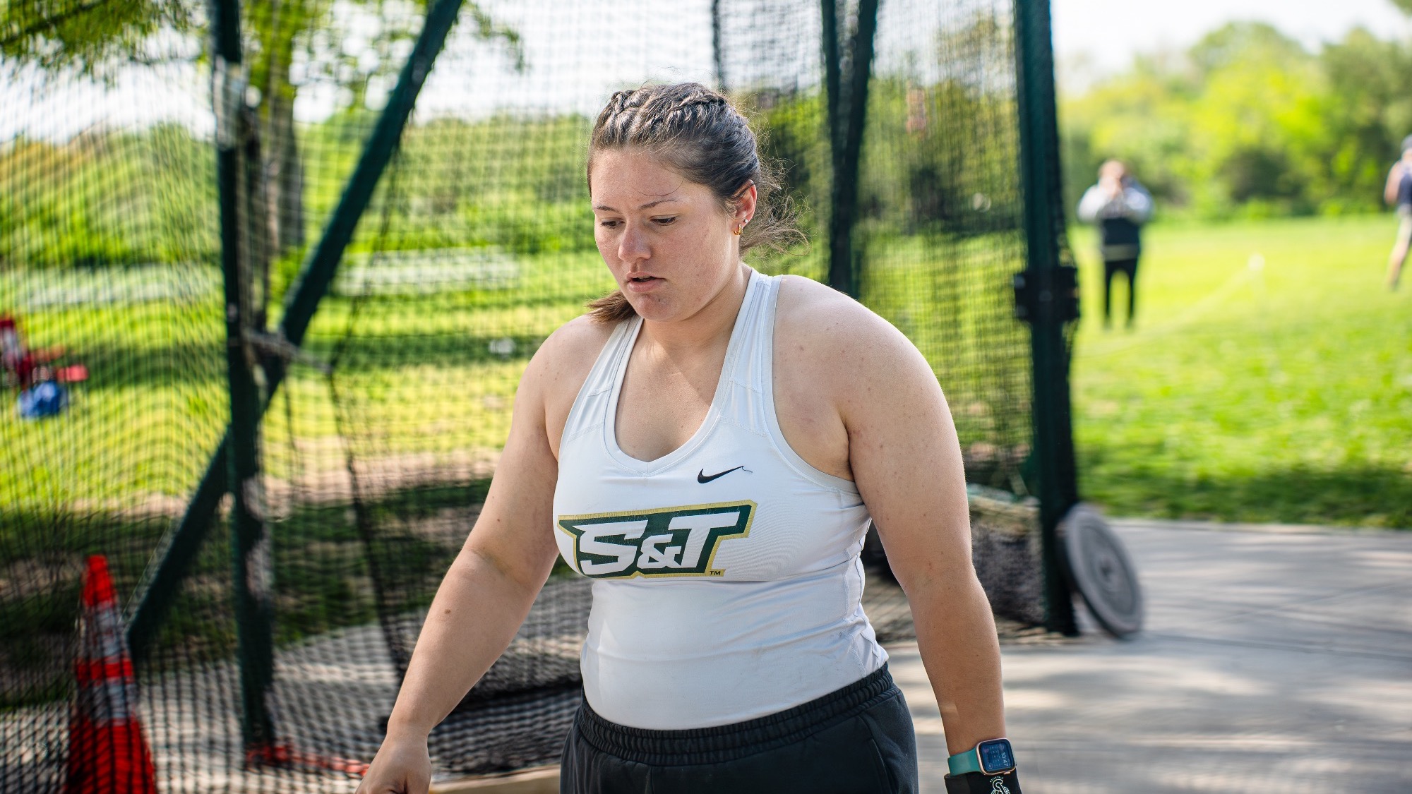 Missouri S&T thrower Madelaine Fischer in her white S&T jersey walking in the throws area outside.