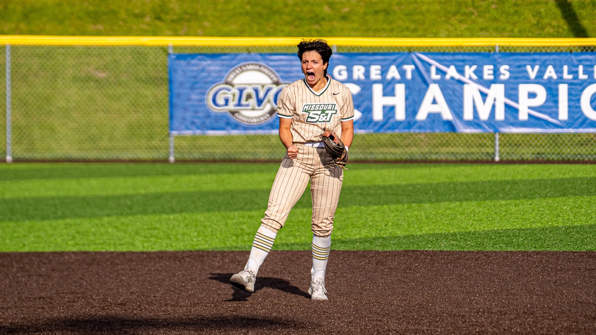 Missouri S&T shortstop Taylor Nelson in pin stripe gold jersey celebrating after her pitcher AJ Agers gets a strikeout on the field during the GLVC Championship Tournament.