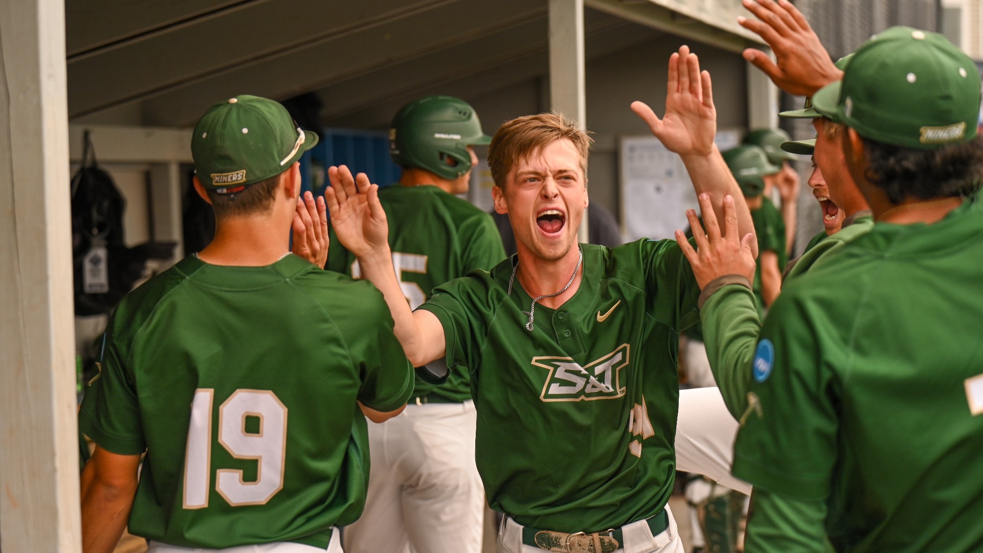 Will Muench of Missouri S&T Baseball photographed celebrating in the dugout with teammates after scoring a run