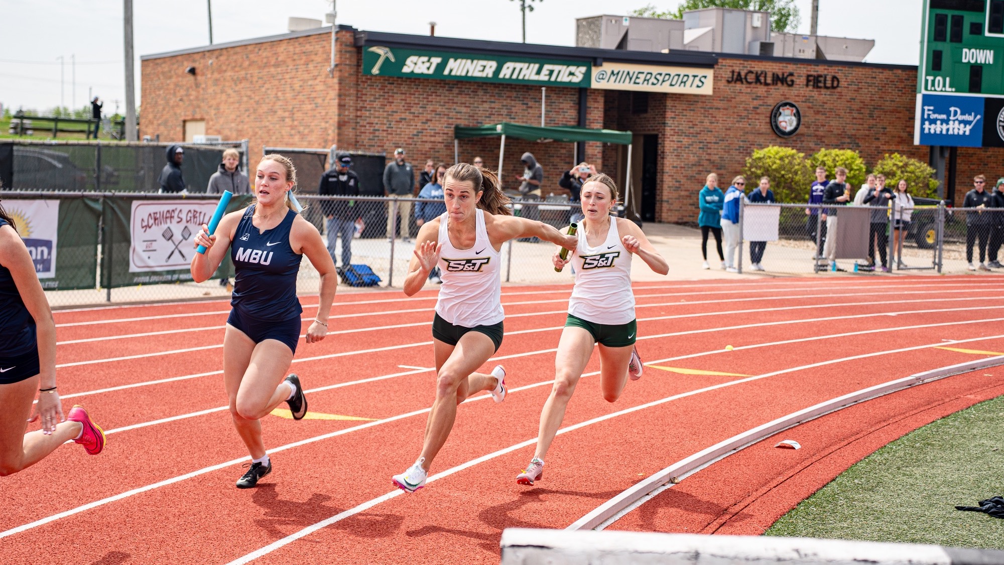 Mary Kimmerle of Missouri S&T running in the 4x100 at the Dewey Allgood Invitational at Missouri S&T with spectators watching in the background.