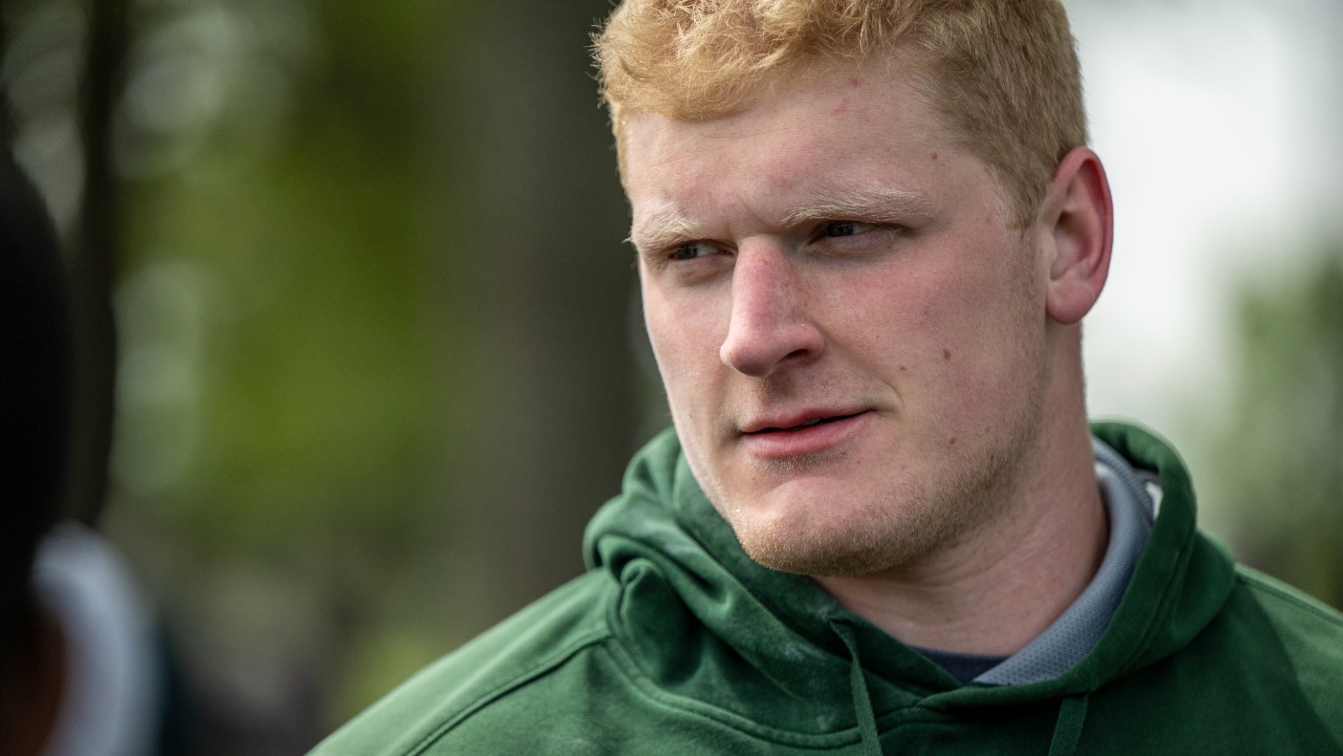 Owen Fraser of Missouri S&T Track and Field photographed while wearing a dark green hoodie. It is a close up portrait as he looks off to his right.