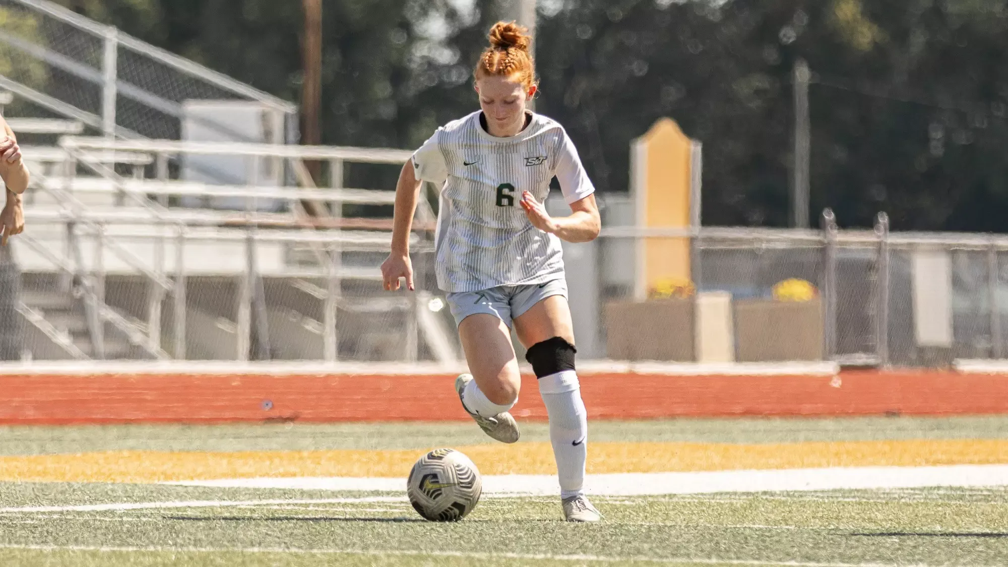 Aubrey Case for Missouri S&T women's soccer team in a white uniform with the number 6 runs toward a soccer ball on an outdoor turf field.