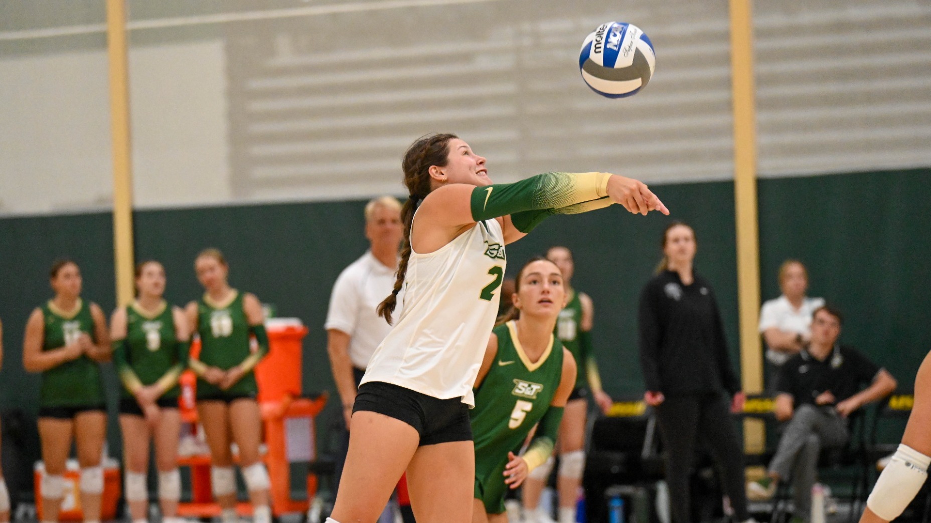 Adelyn Weiler at MSSU Tournament in the process of digging the volleyball. She is wearing a white uniform with black shorts and knee pads
