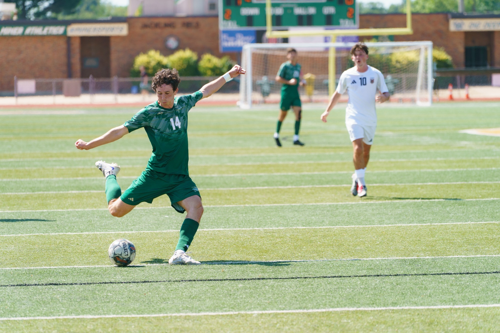 Caleb Lepant in a green Missouri S&T jersey winds up to punt a soccer ball. 