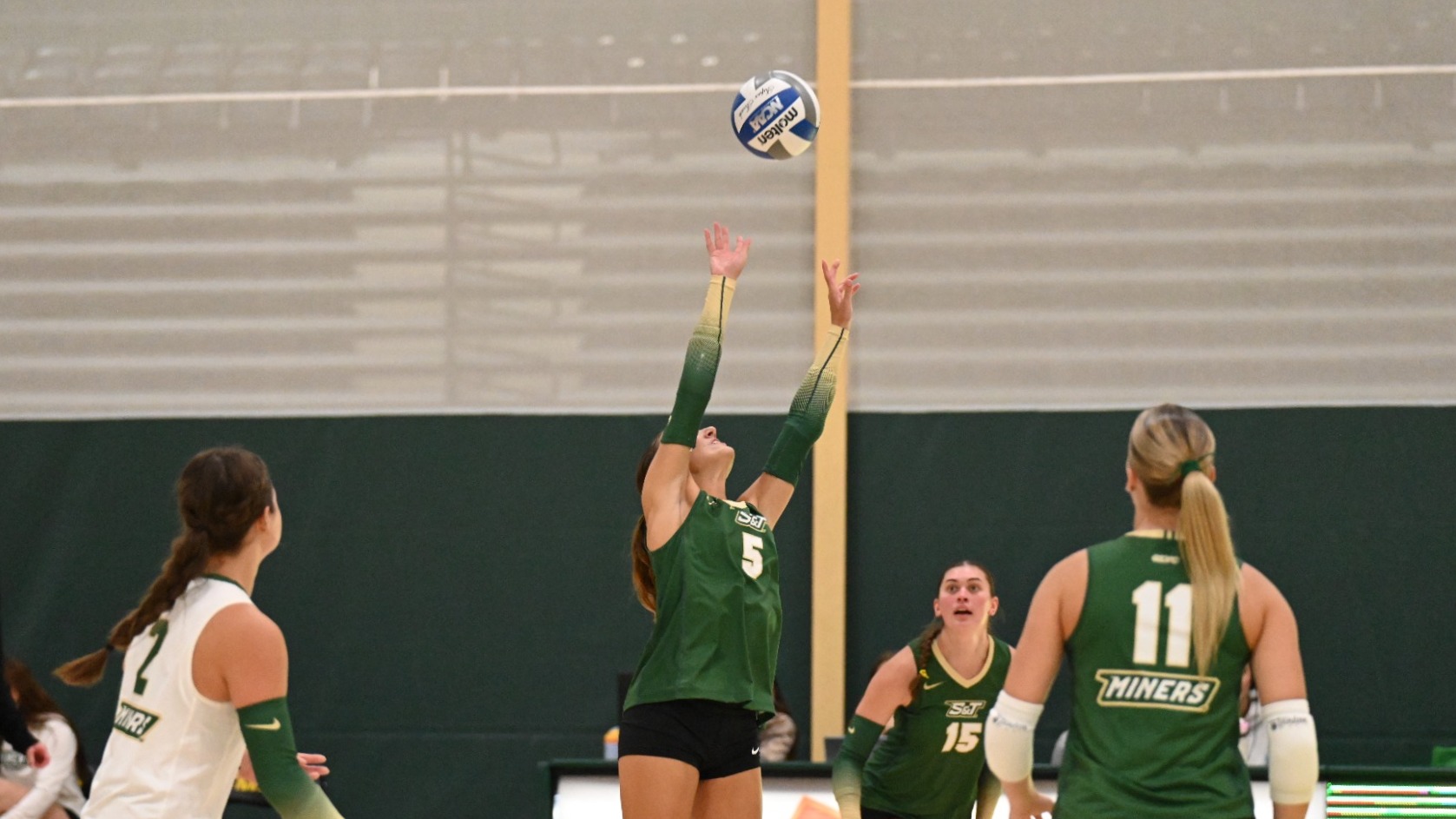 Chelsea Plunkett of Missouri S&T Women's Volleyball is photographed setting the ball during a match at MSSU. She is wearing a green uniform.
