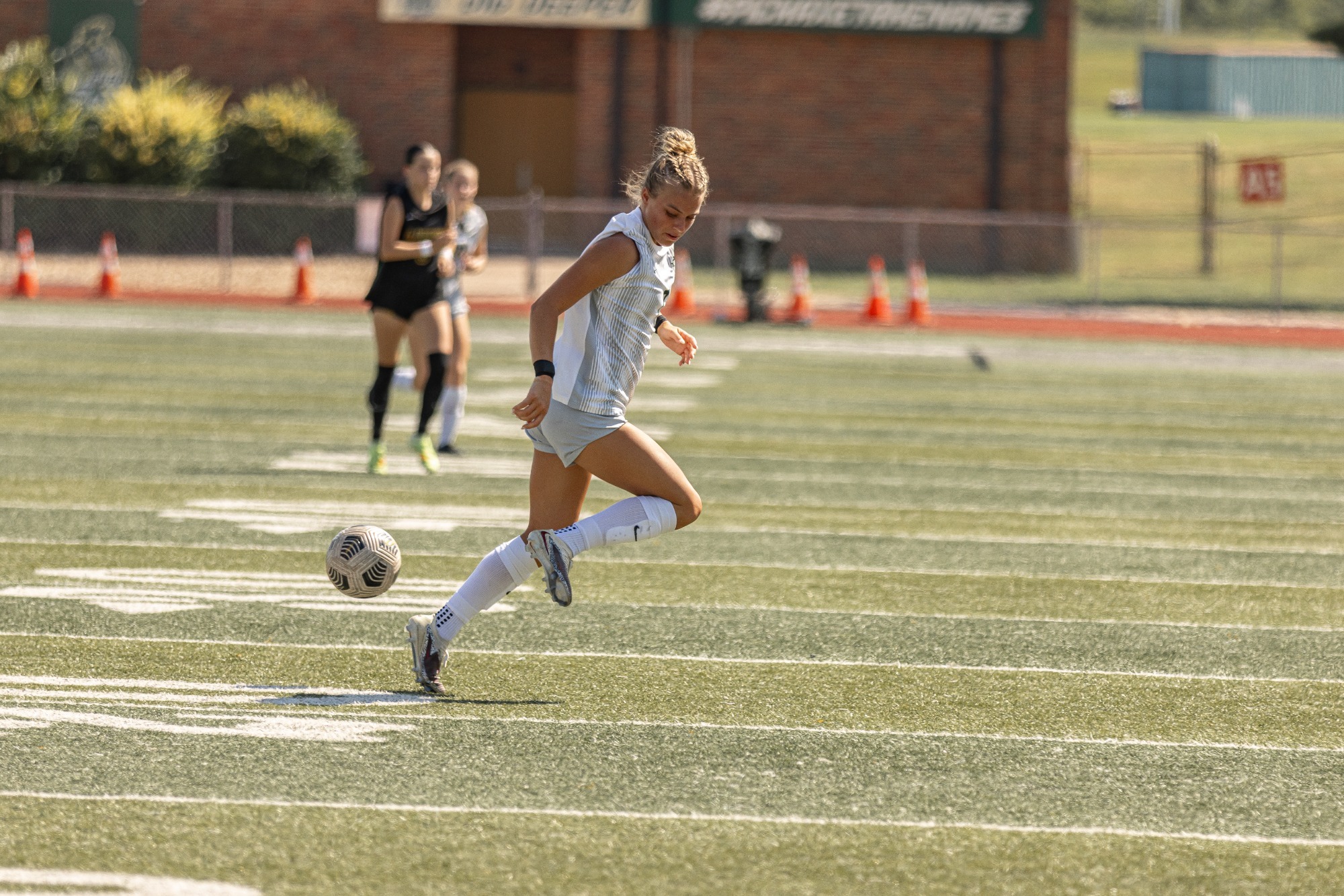 A Missouri S&T women's soccer player looking back at the soccer ball in a white uniform. 