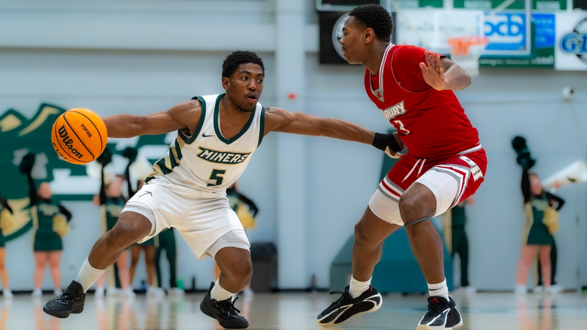 Darron Henry of Missouri S&T Men's Basketball photographed wearing a white uniform and dribbling the basketball past a Drury defender during a game in Gibson Arena. 