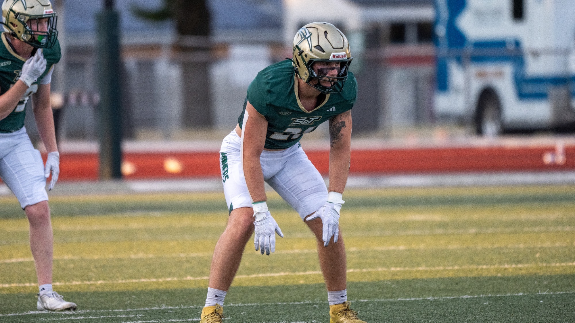 Cameron Sturgell of Missouri S&T football photographed wearing a green jersey with white pants and a gold helmet. He stands ready for the next snap during a game at Allgood-Bailey Stadium