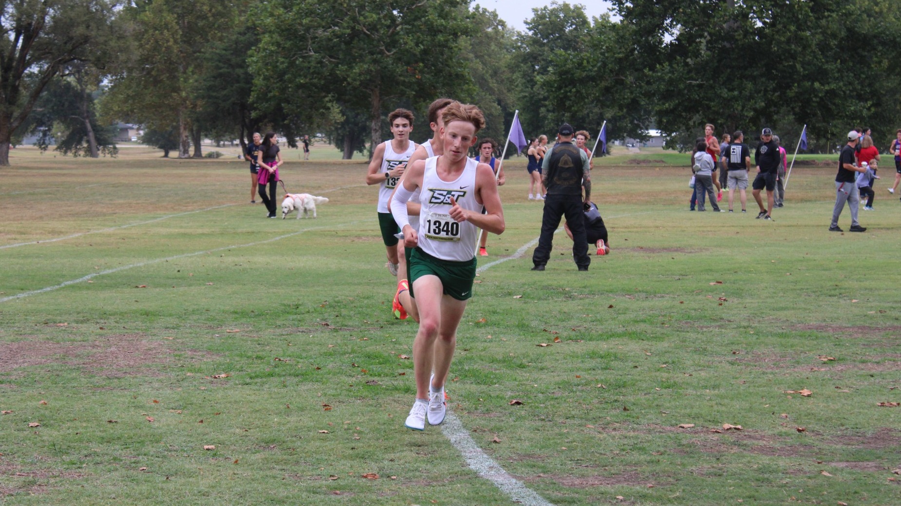 Spencer Pye of Missouri S&T Men's Cross Country photographed rounding a corner while running at a meet and wearing a white uniform with green shorts