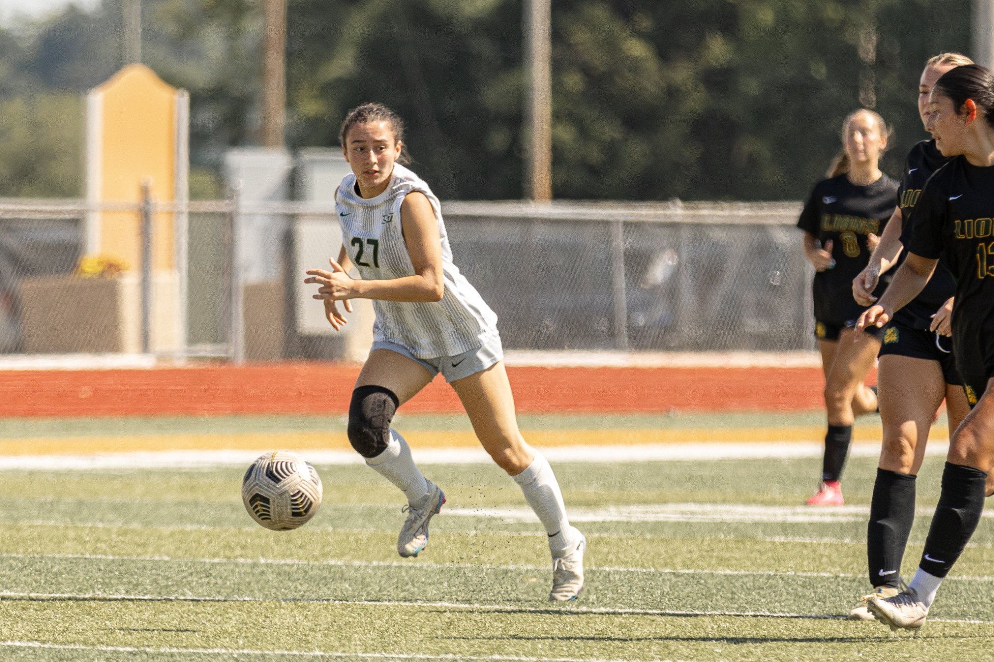 Nathalie Bello in a white jersey and white shorts for Missouri S&T running with the ball to escape Missouri Southern's defense in black jerseys and black shorts