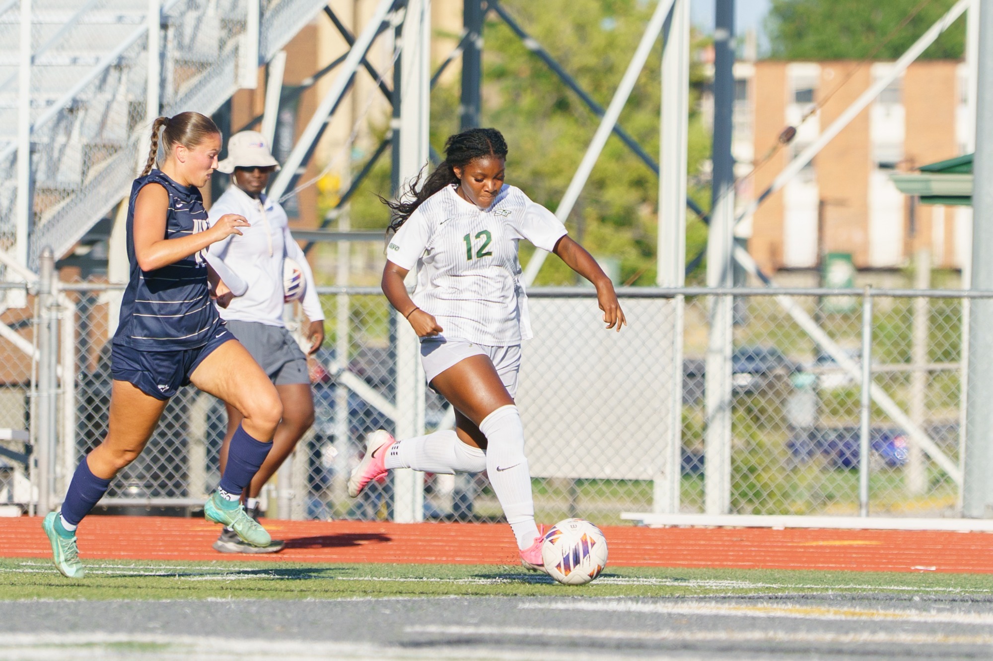Jordan Williams for the Miners in a white jersey and white shorts kicking the ball away from a defender and advancing forward.