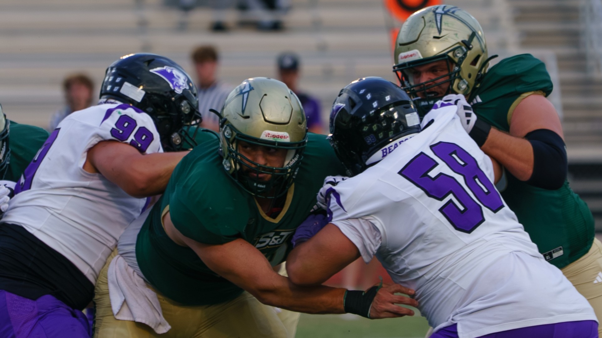 Nadeem Ayoub of Missouri S&T Football photographed wearing a green uniform and gold helmet blocking SBU defenders during a field goal attempt