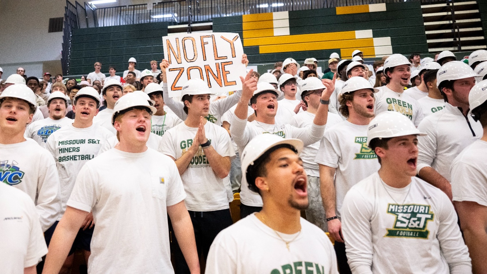 Pickaxe Platoon student-athletes cheering during a basketball game in Gibson Arena. They are wearing white tee shirts and white S&T hard hats