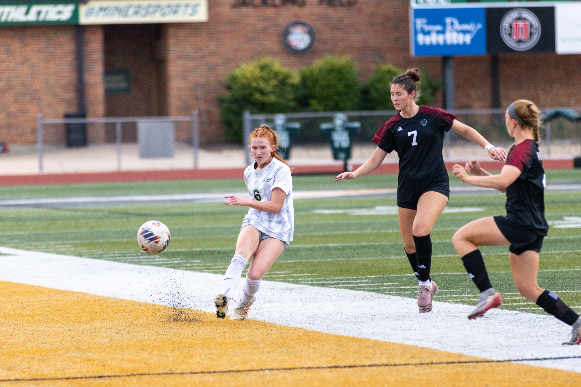 Aubrey Case in a white jersey and white shorts punting the soccer field towards the camera