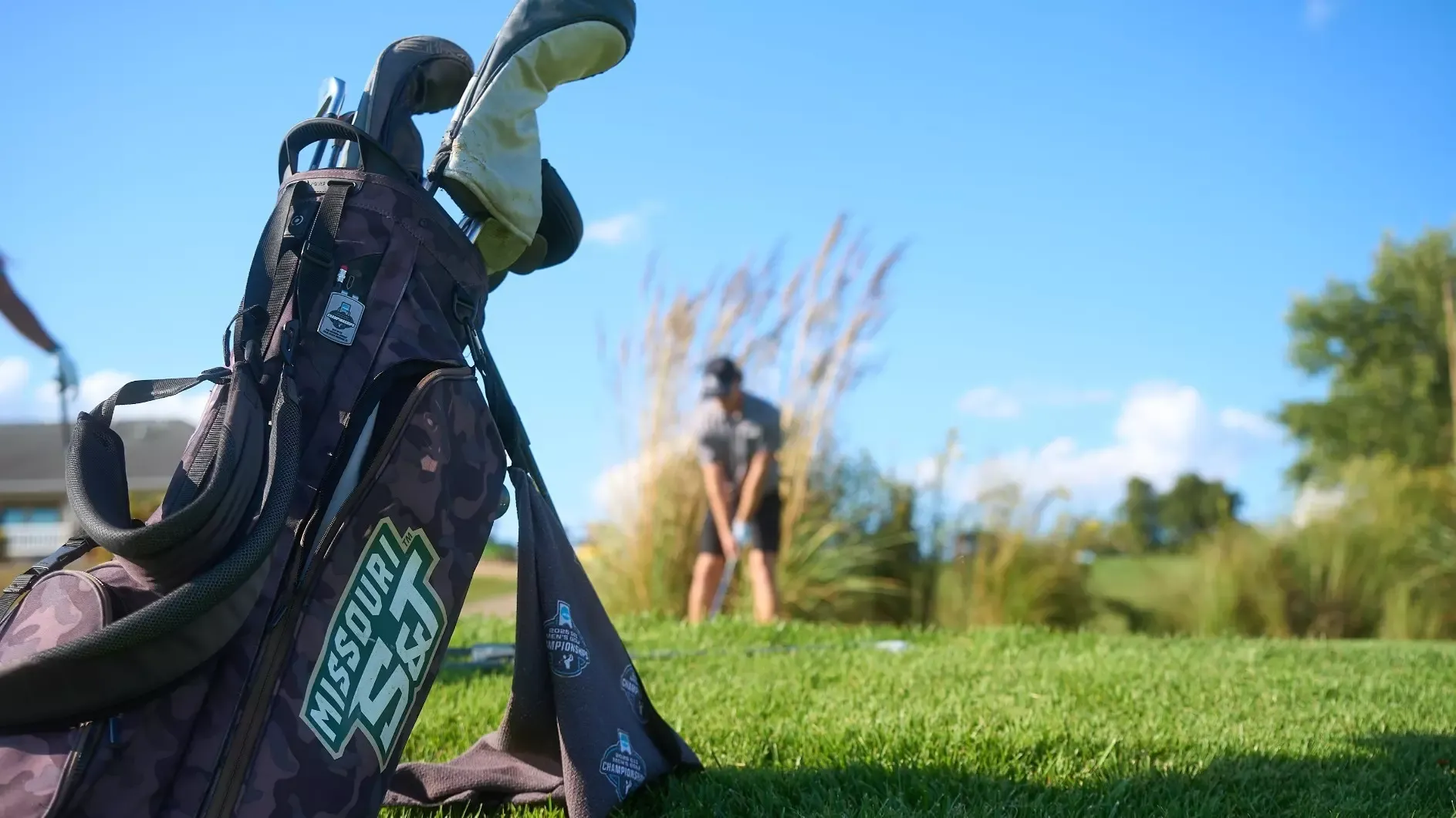 Missouri S&T Golf Bag photographed out at the golf course with a Miner golfer out of focus taking a tee shot in the background