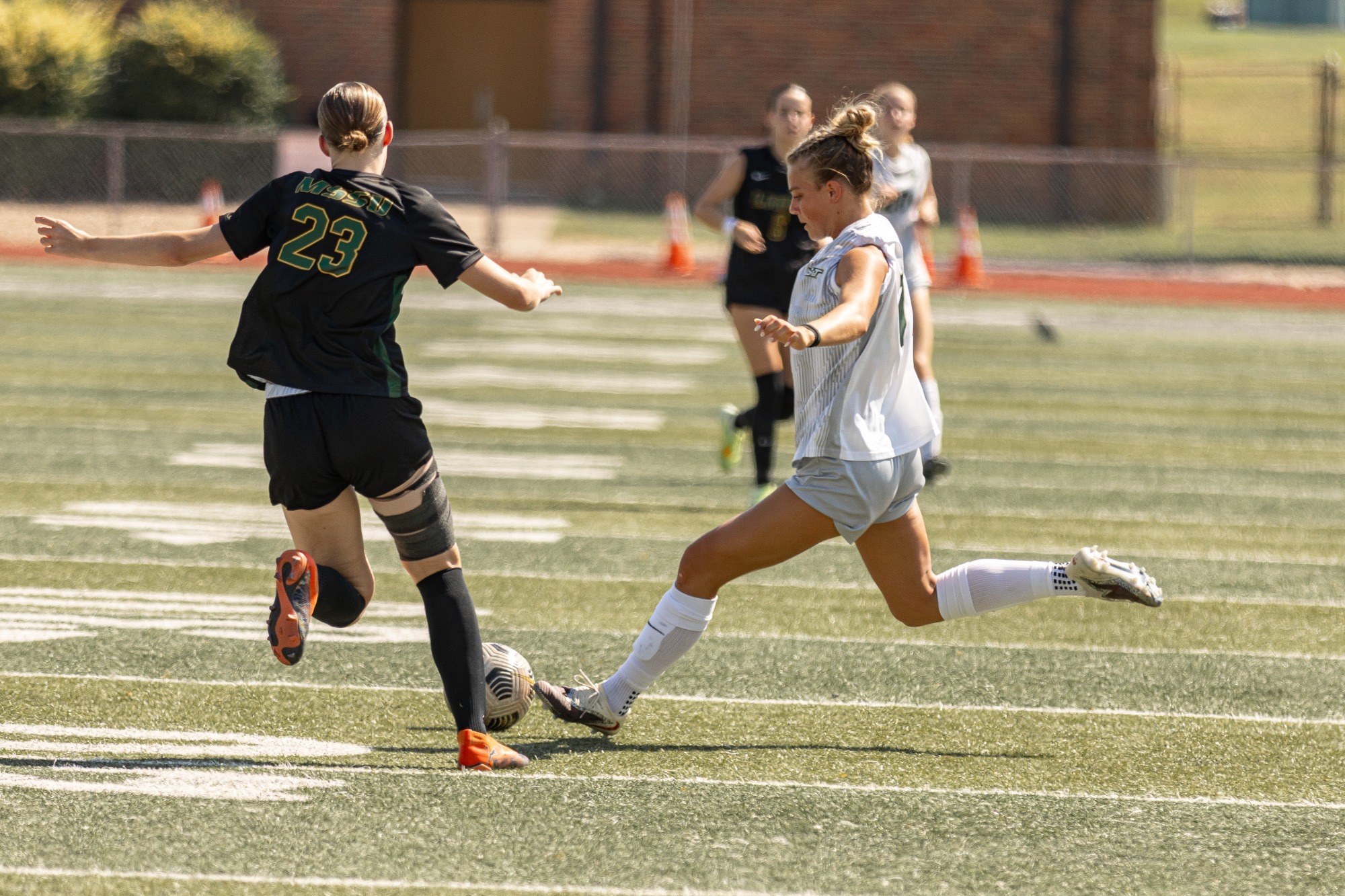 S&T Women's Soccer player attacking the soccer ball in a white jersery and white shorts, avoiding a defending player in a black jersey and black shorts