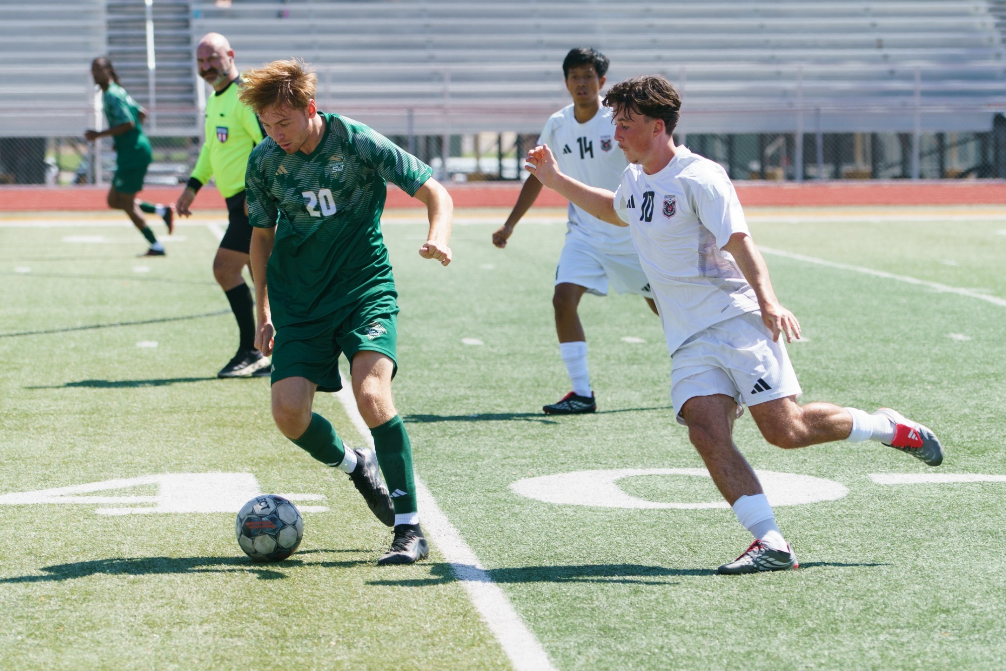 Logan Wallace in a green jersey and green shorts defending the soccer ball from a Davenport player in a white jersey with white shorts