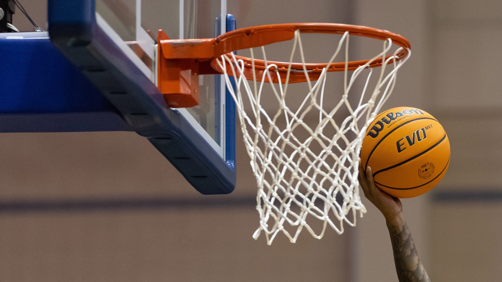 Basketball hoop with a ball in the hand going in for a layup