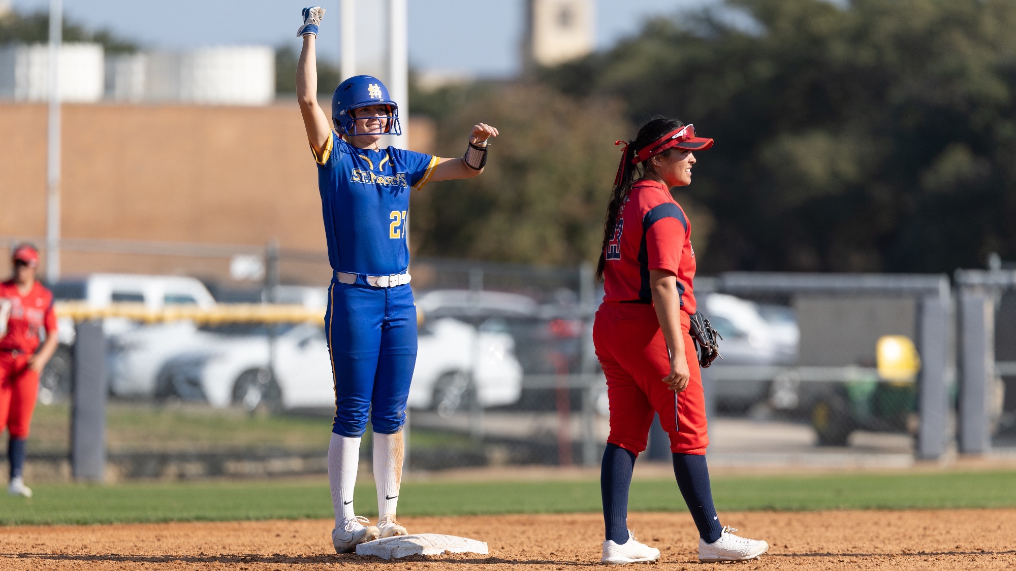 Raegan Tennill stands on second base with one fist raised above her and the other pointing to her teammates in the dugout in celebration.
