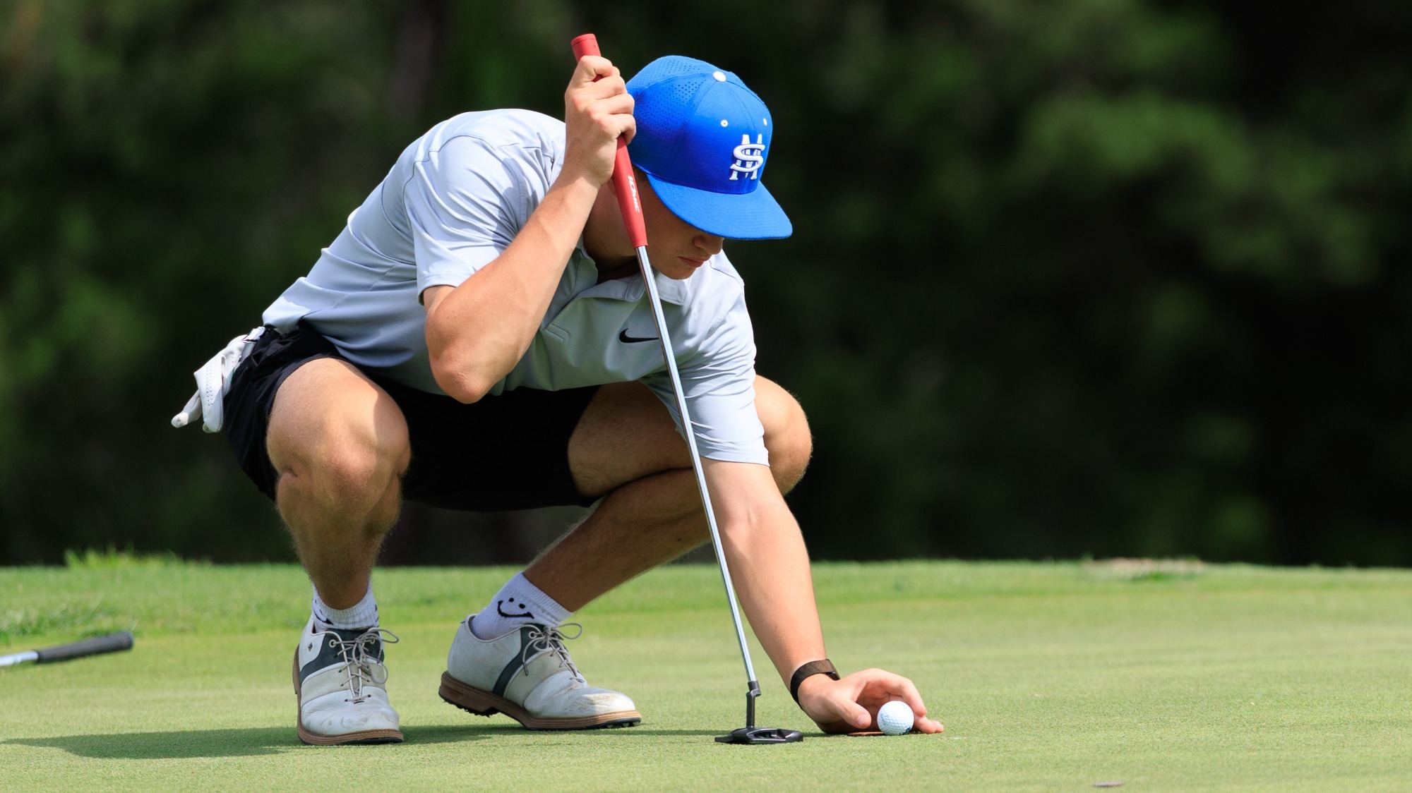 Matthew Lewis squats down to place his ball on the green at TPC.