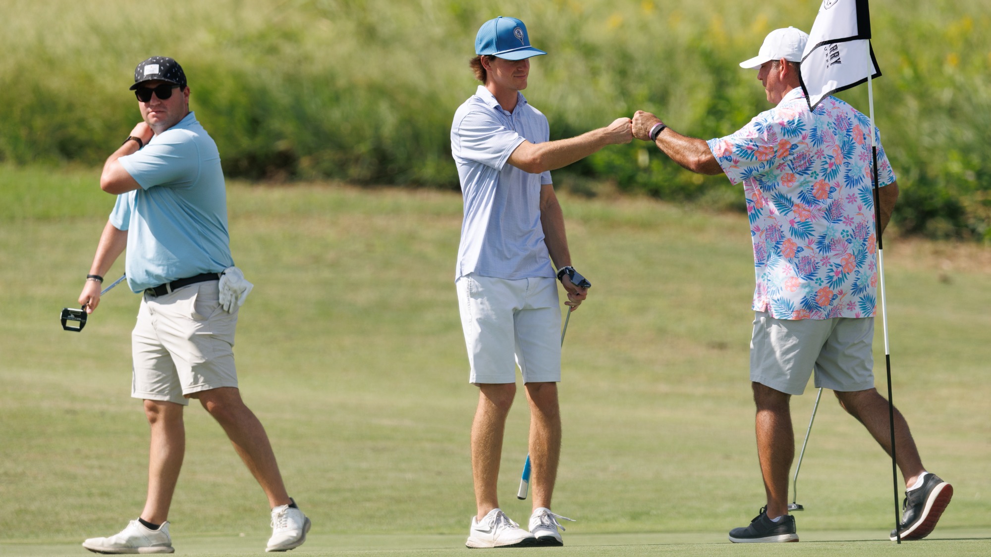Father and son fist bumping after a putt with a male golfer behind them.