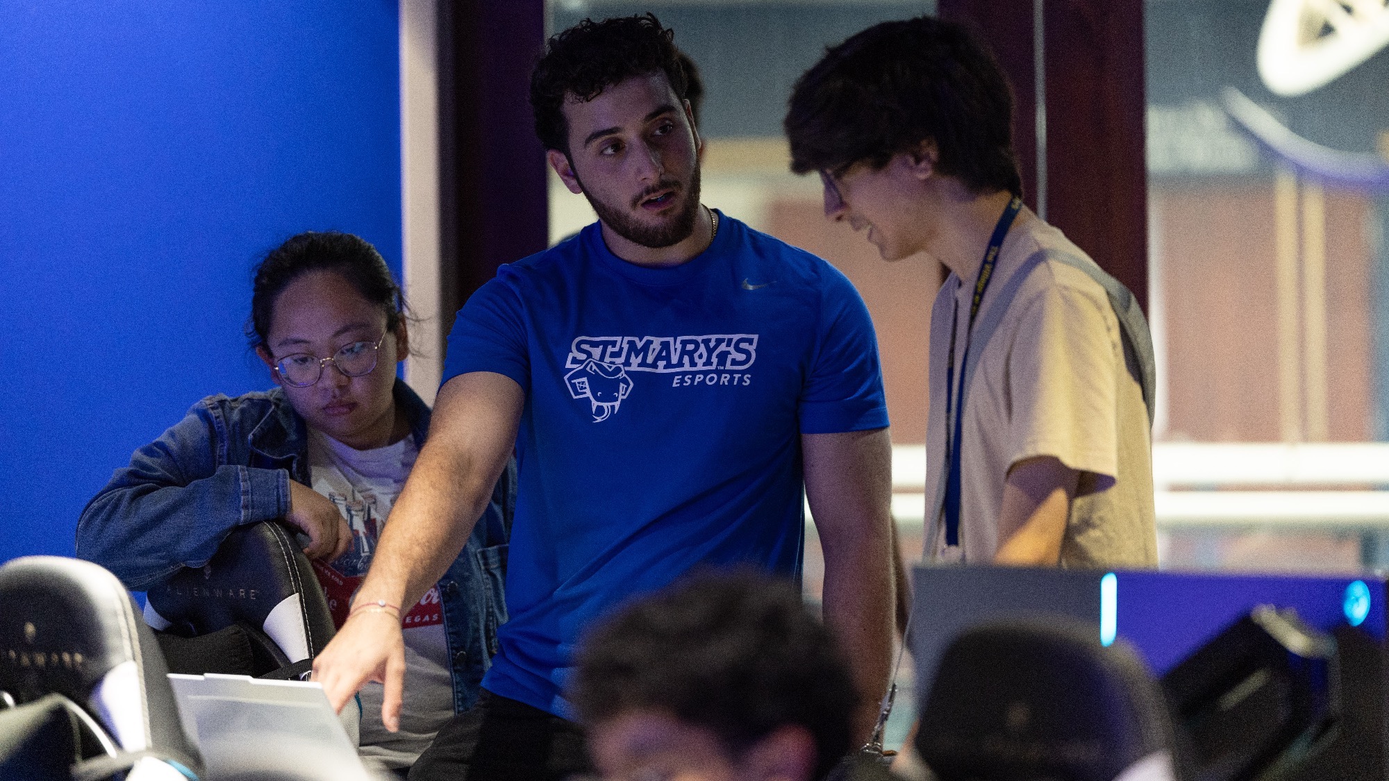 David Kamel points at a computer screen, while talking with a teammate. Assistant Coach Franchesca Tinacba sits nearby, listening.