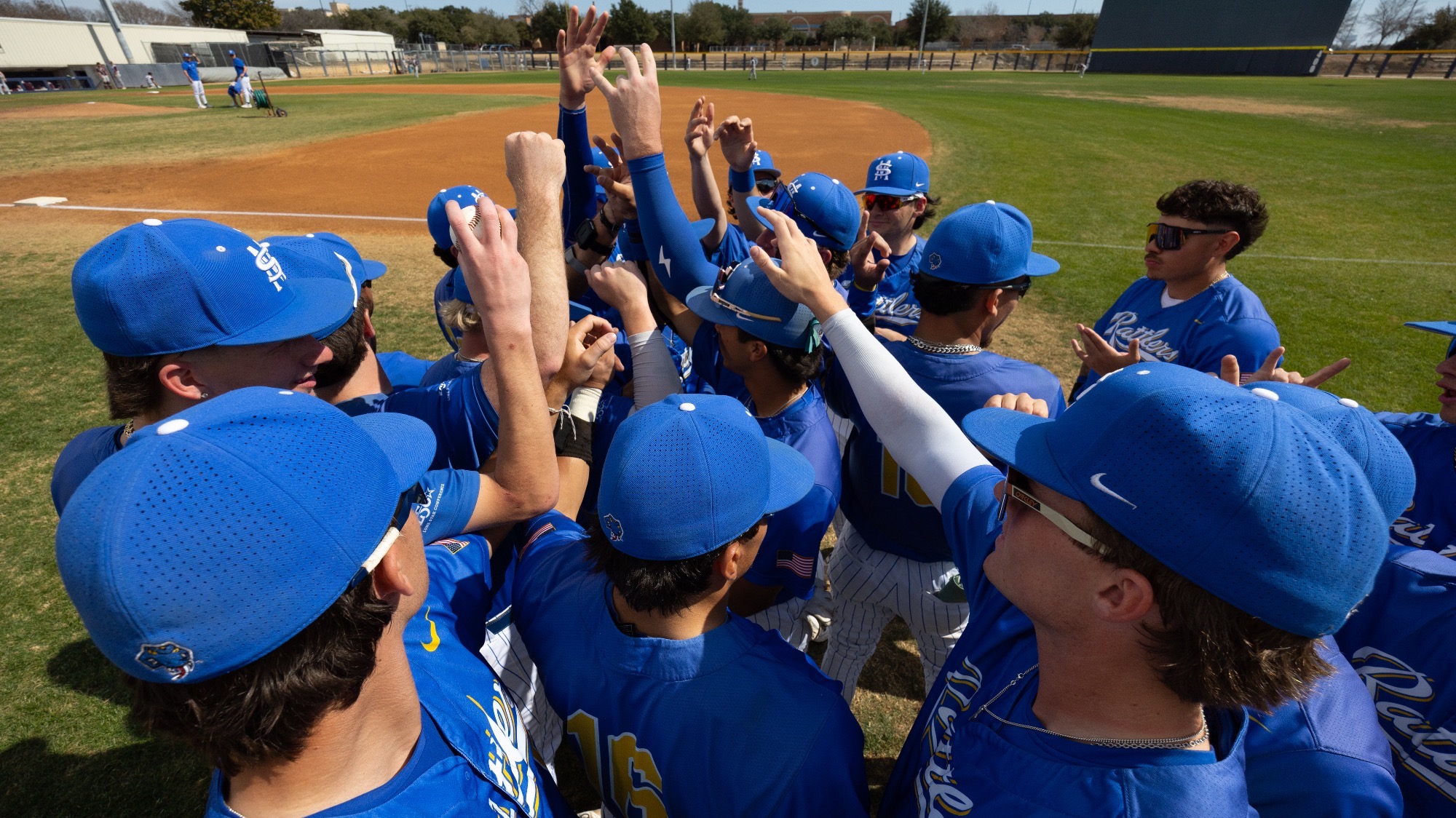 The baseball team huddles with hands up.