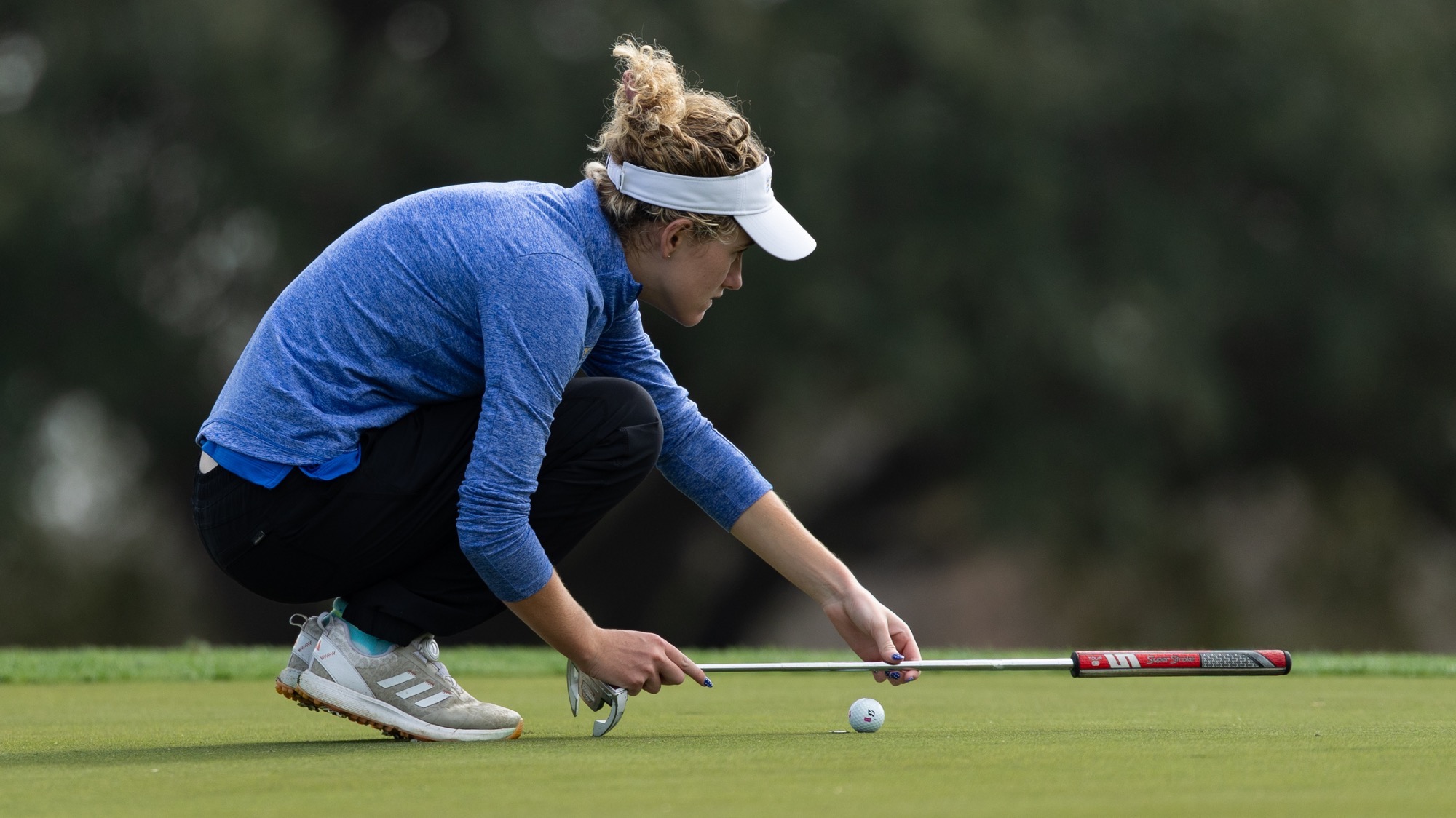 Brielle Burns squats down and measures with her putter.