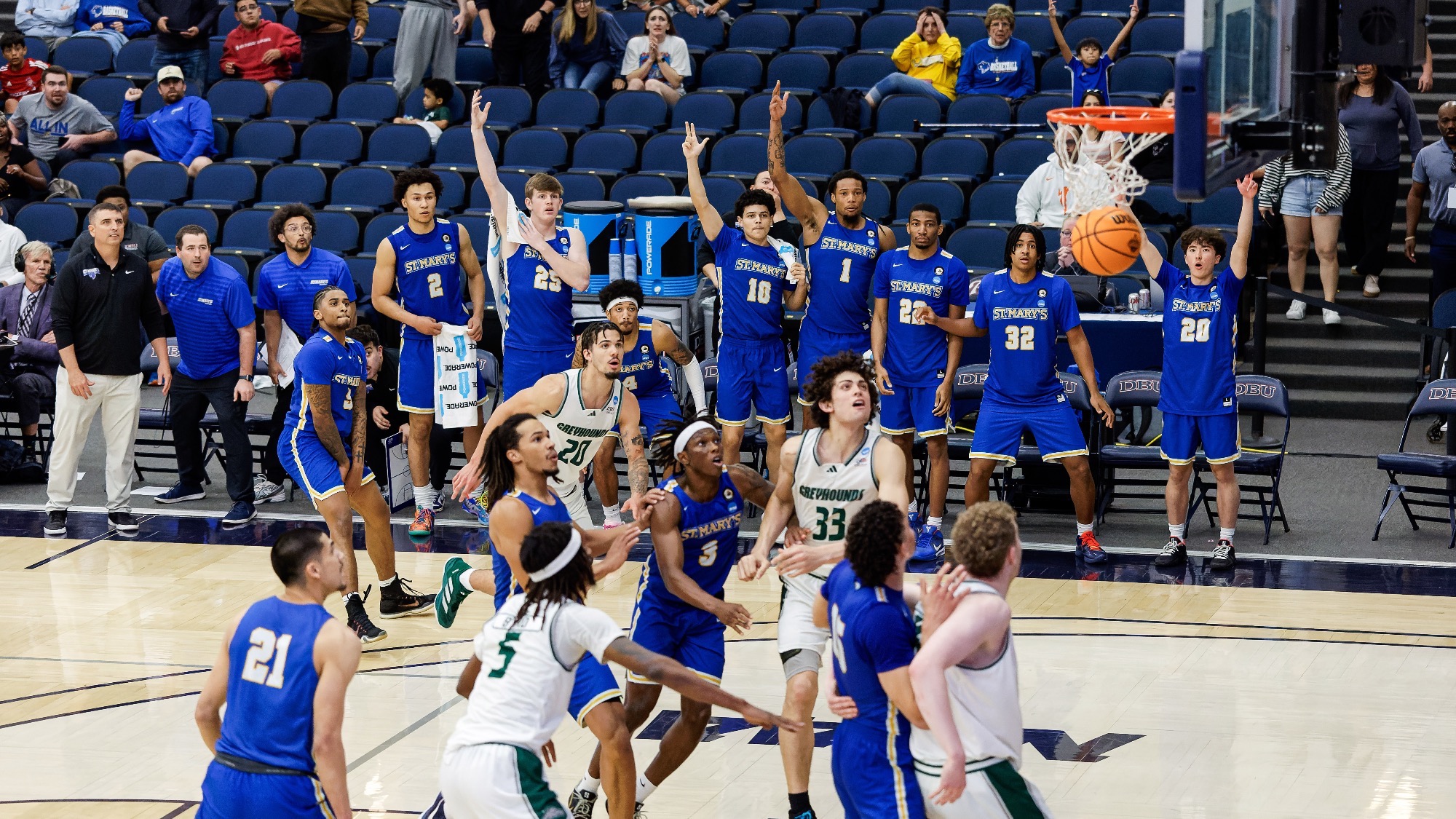 Damani Claxton stands outside the arc after making the game winner with 3.3 seconds remaining. The remaining players box each other out under the rim, while the bench looks on with hands raised.