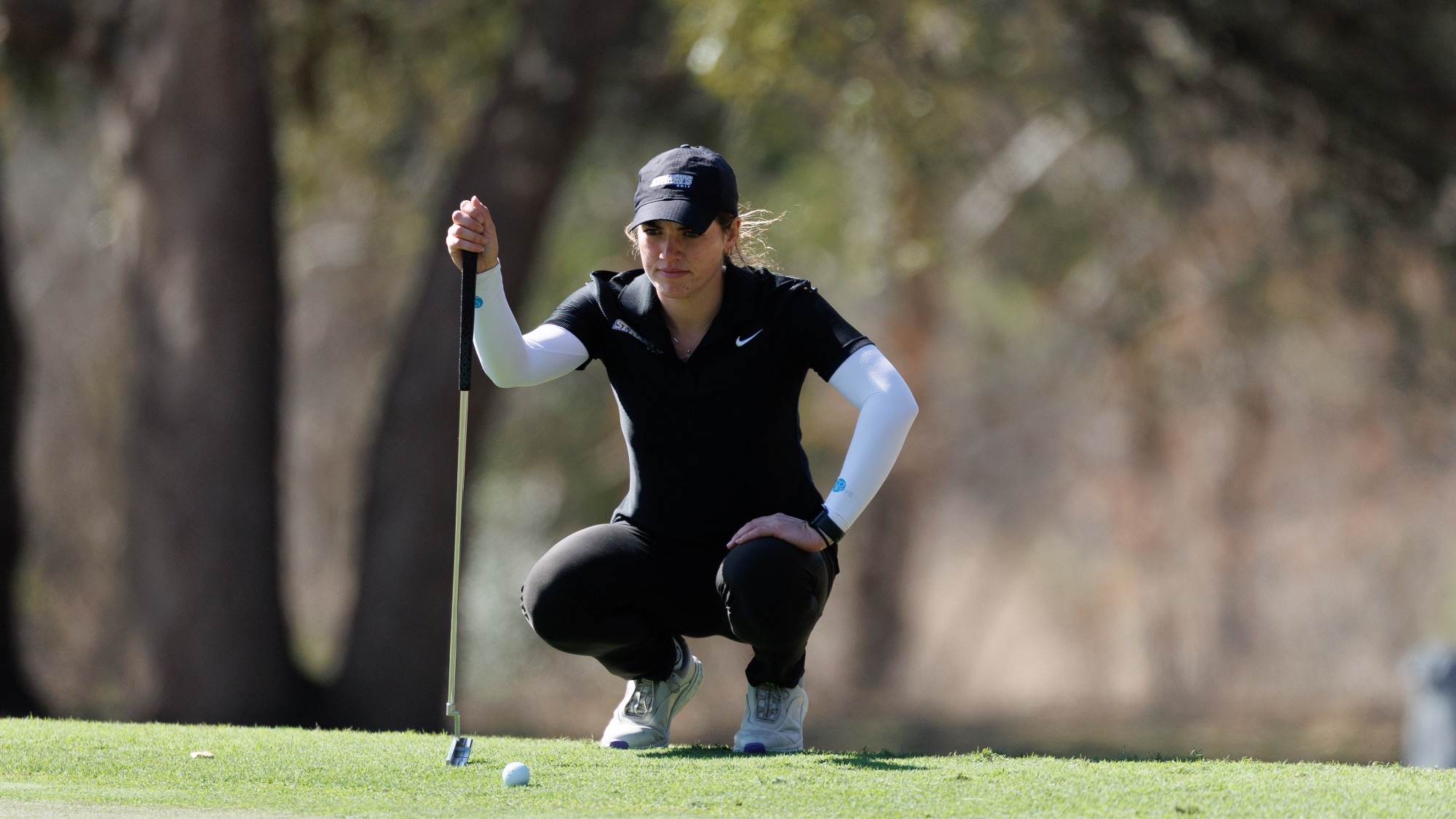 Sophia Perkins squats down with putter in right hand to get a look at the lie on the green.