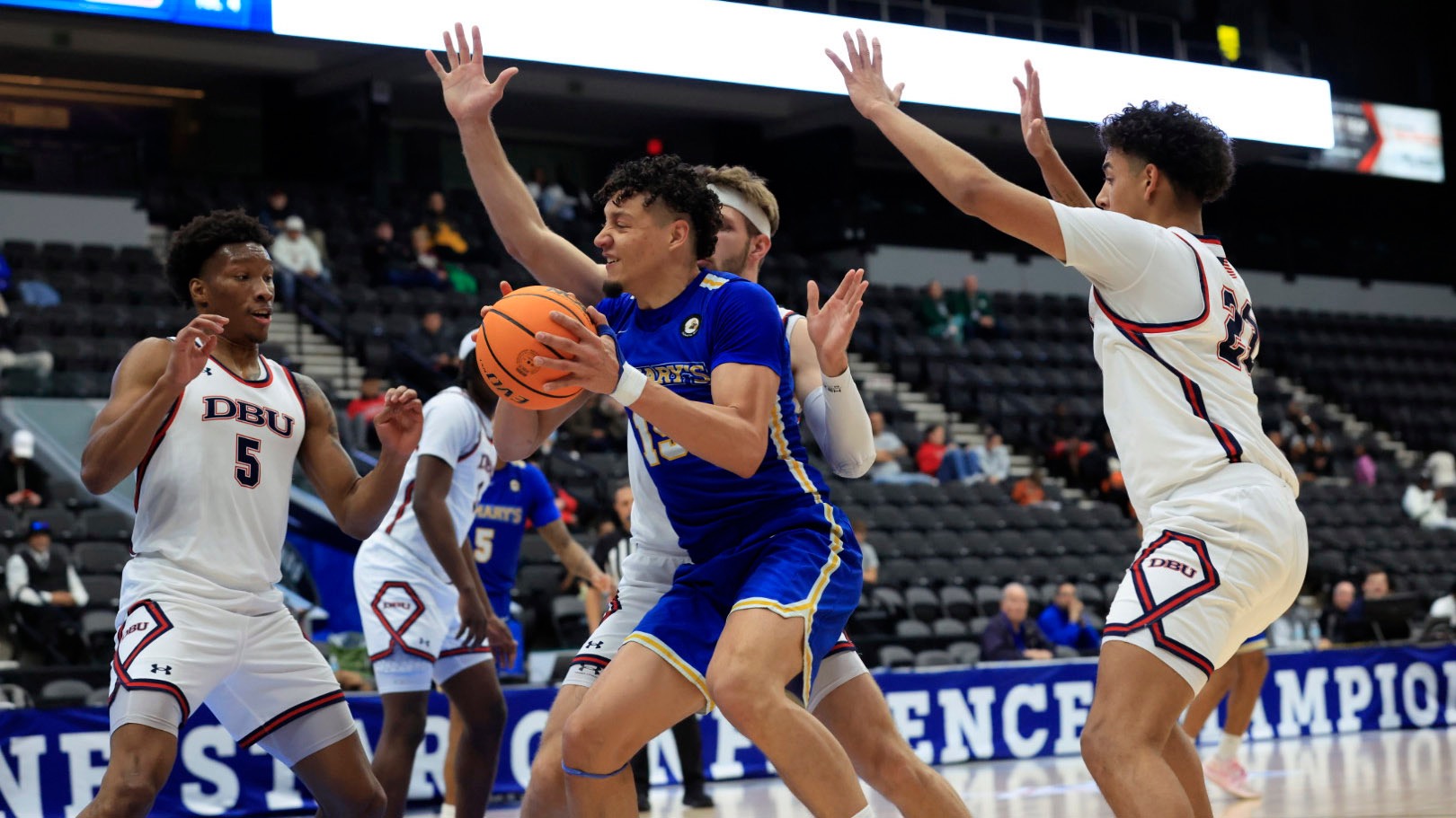 Olaverr Camacho holds the ball at his chest while four DBU players converge around him.
