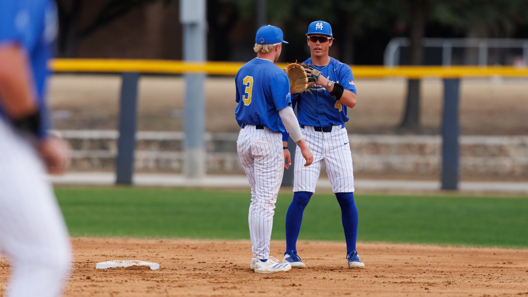 Ashton Beiard and Blake Allen slap gloves as they stand over second base and discuss strategy.