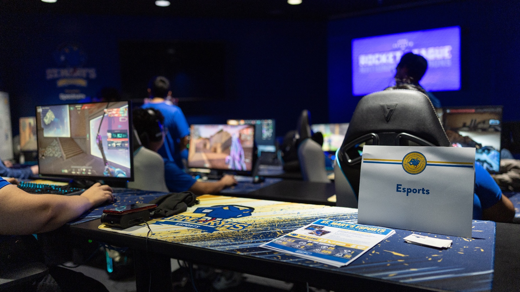 The Esports team fills the room, and each of the visible monitors has a different game/scene on screen.