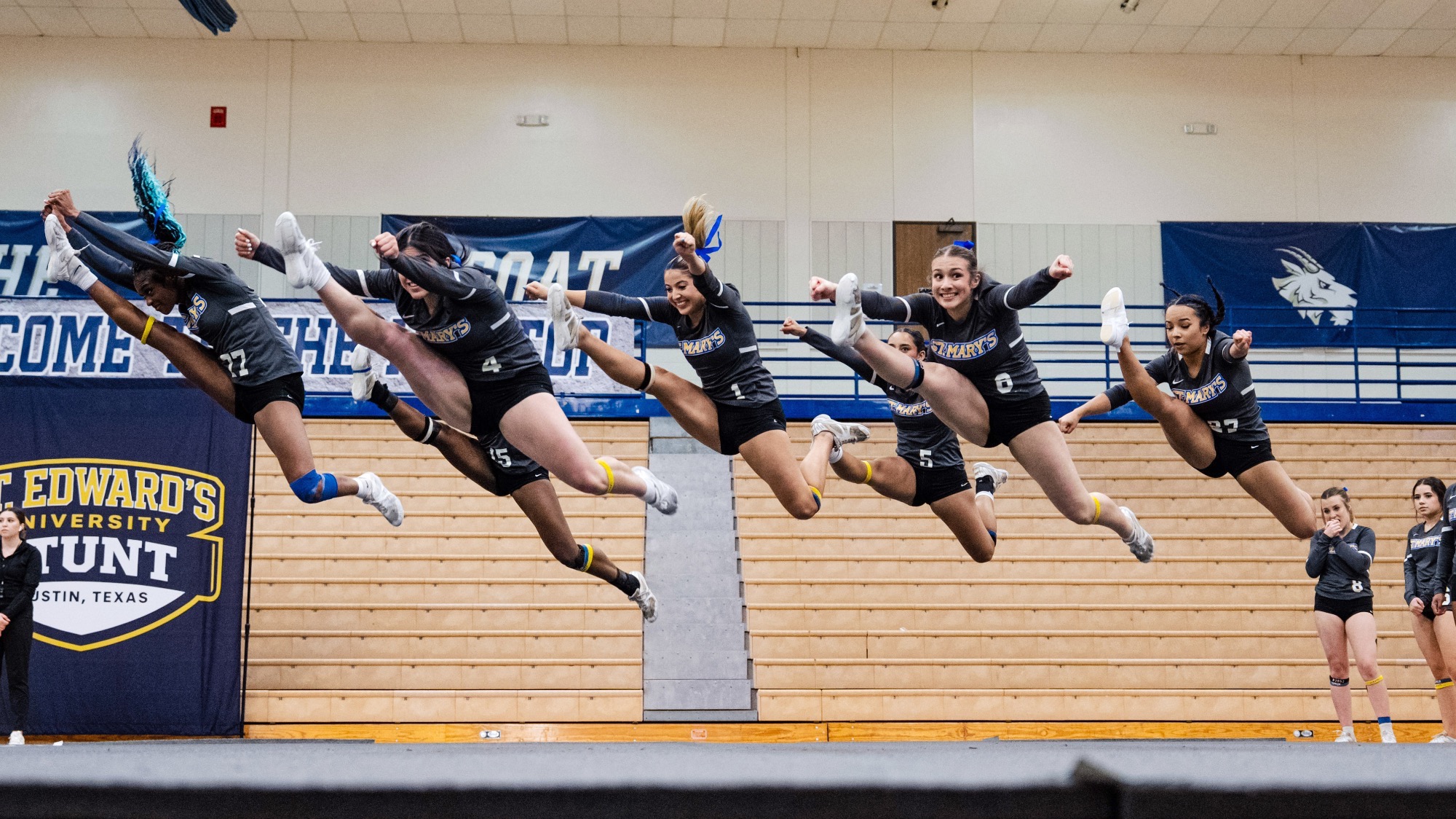 The 2026 STUNT team is in mid-air completing a hurdle jump during the jumps and tumbling quarter.