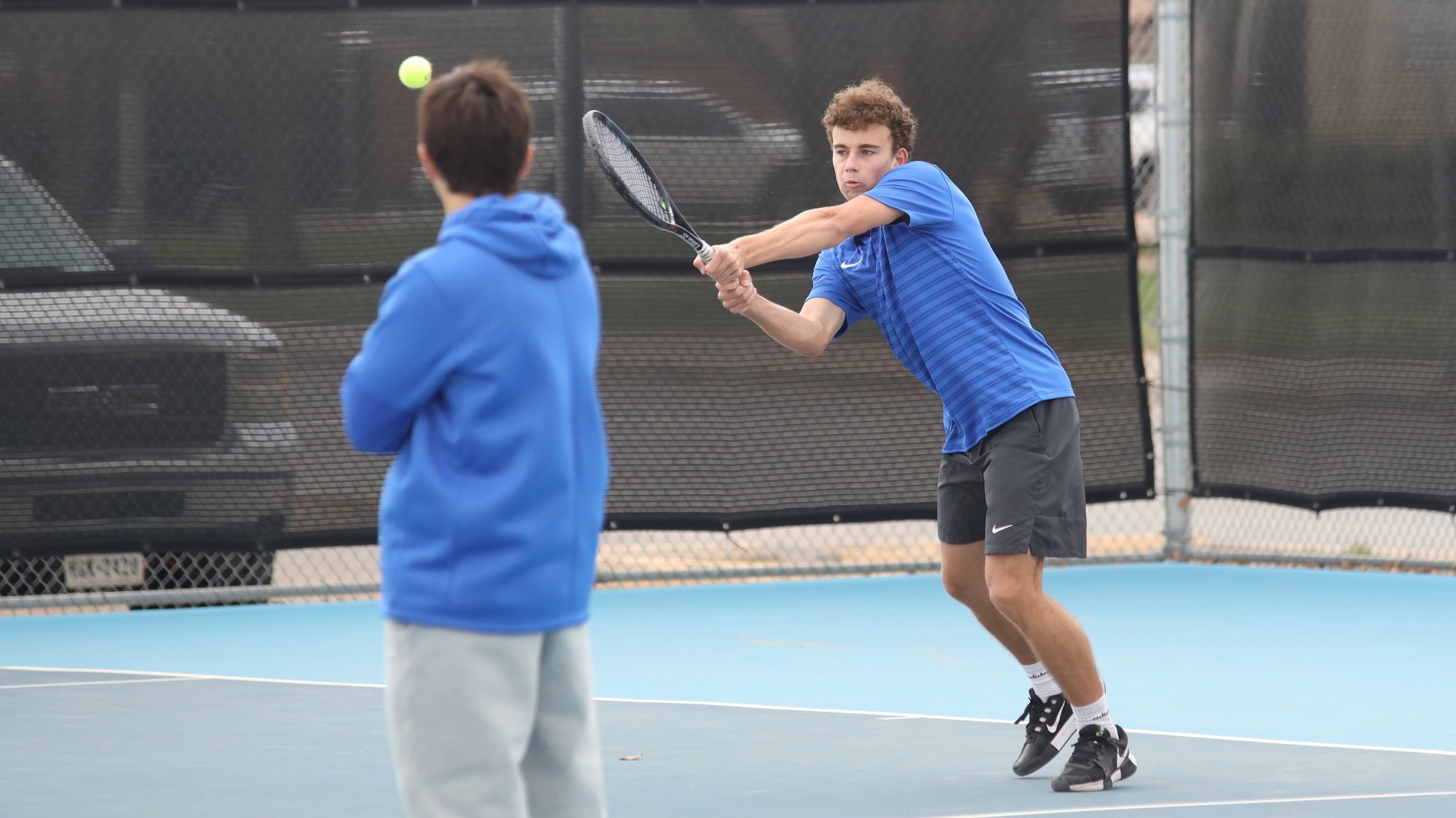 Victor Velter returns a shot with a two-handed backhand at Lubbock Christian, while assistant coach Dakota Fernandez looks on.