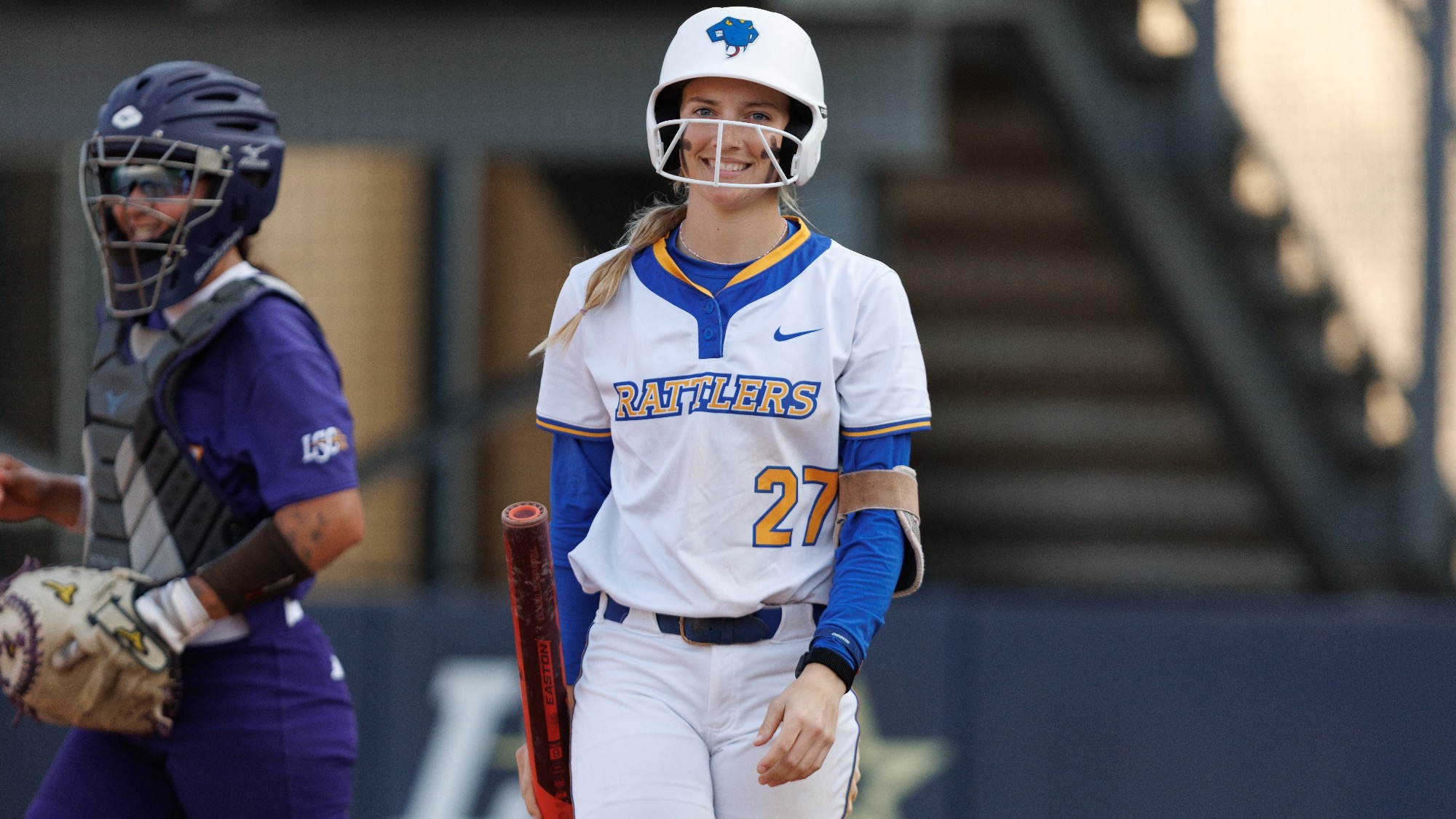 Raegan Tennill smiles at the dugout with the bat in her right hand.