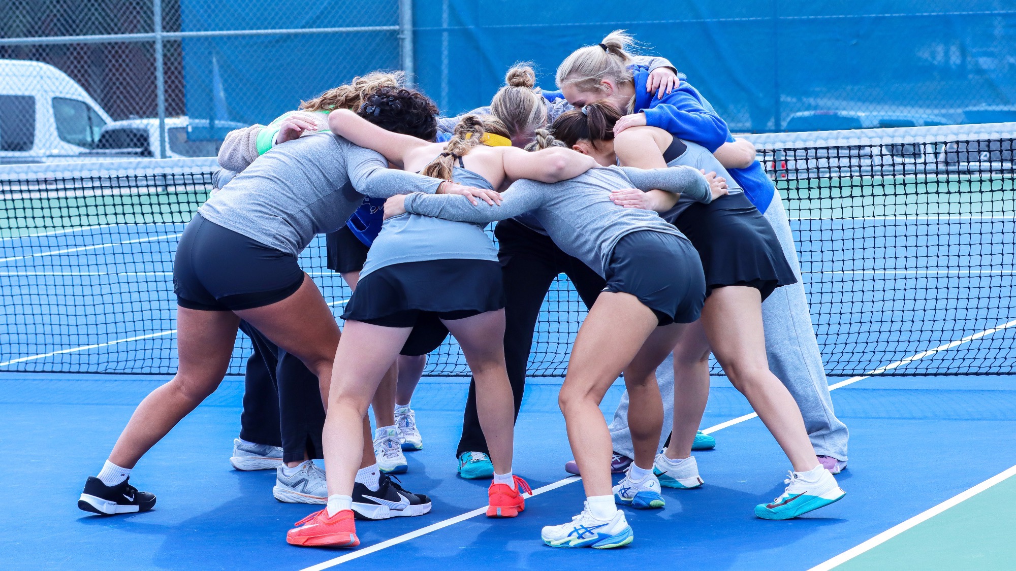 The Women's Tennis team huddles bent over at the waist before beginning the tournament at Texas State.
