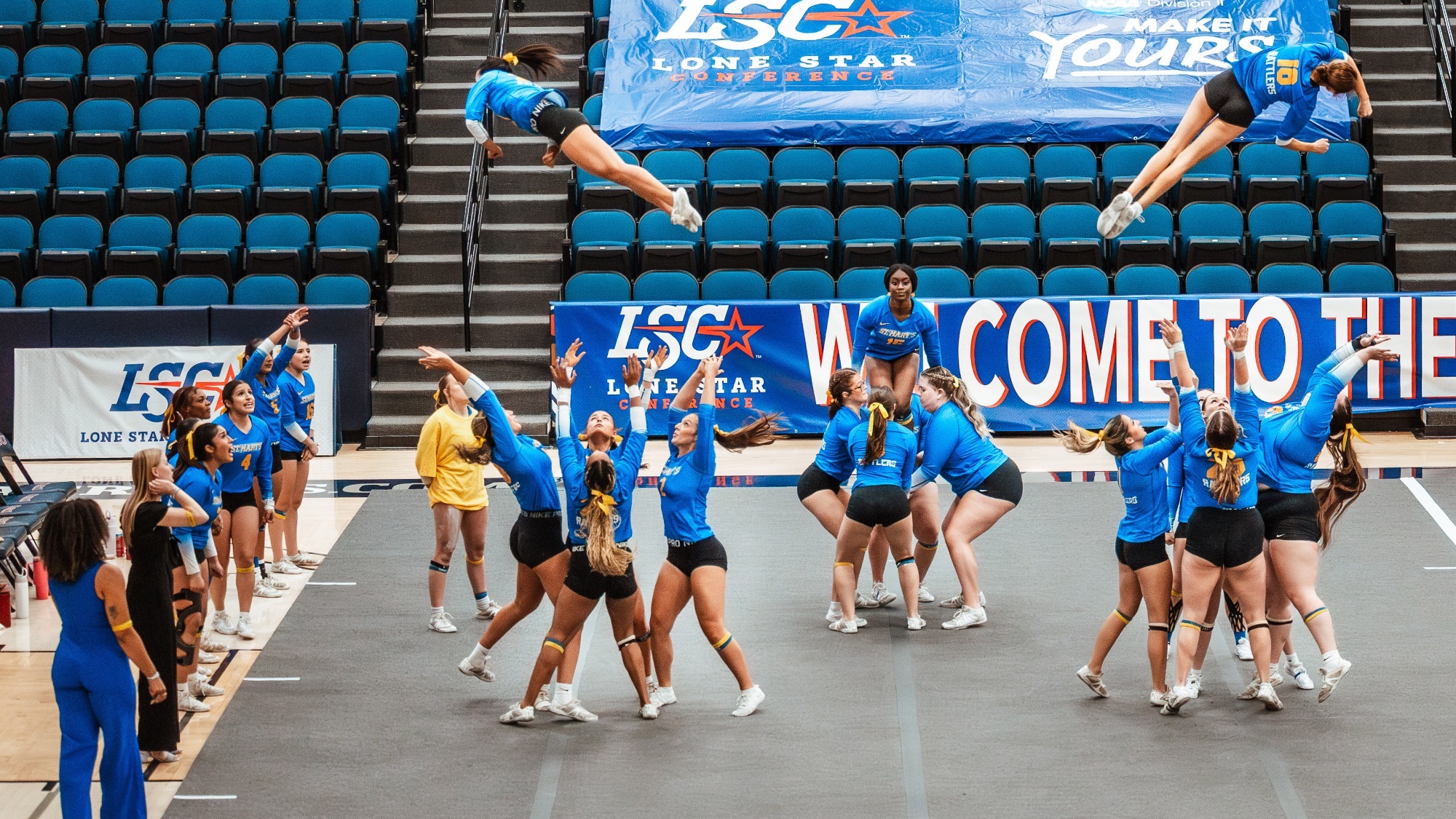 Two groups of STUNT athletes are waiting to catch a twisting athlete, while a third group behind, prepares to toss one in the air.