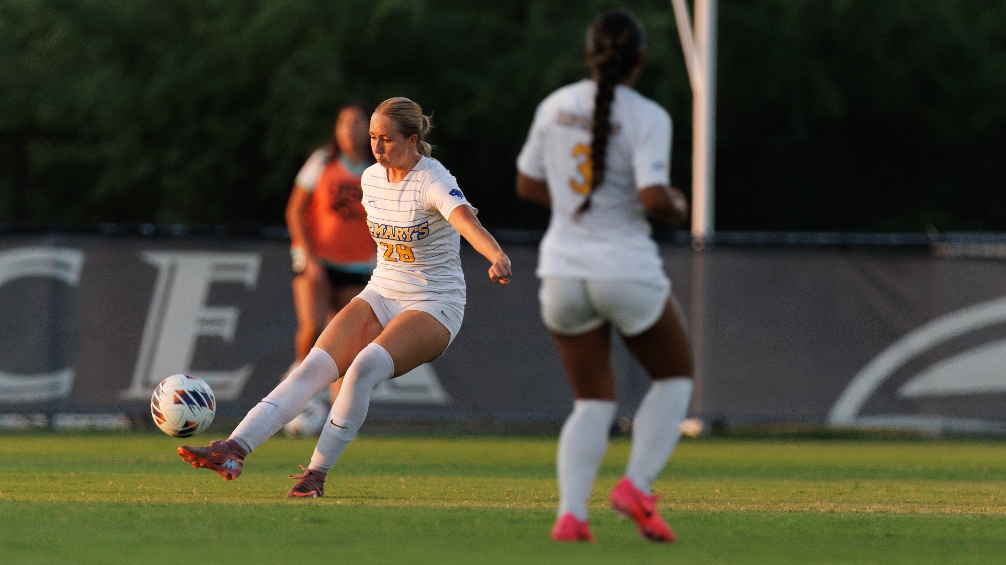 Gracie Van Sluis kicks the ball with Nia Mendiola in the foreground blurry