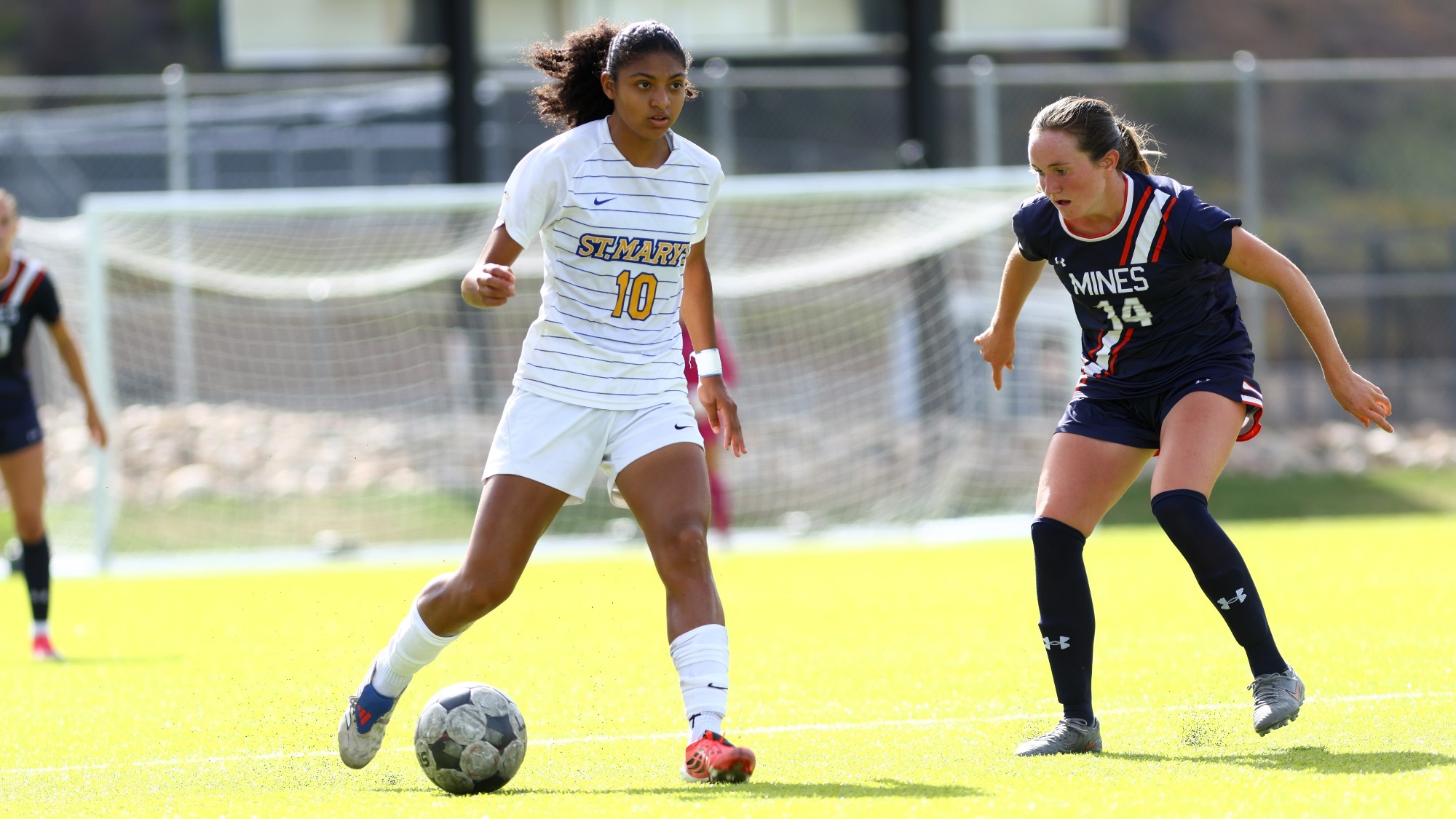 Kamrynn Martinez looks up the pitch as she dribbles the ball with a defender on her left hip.