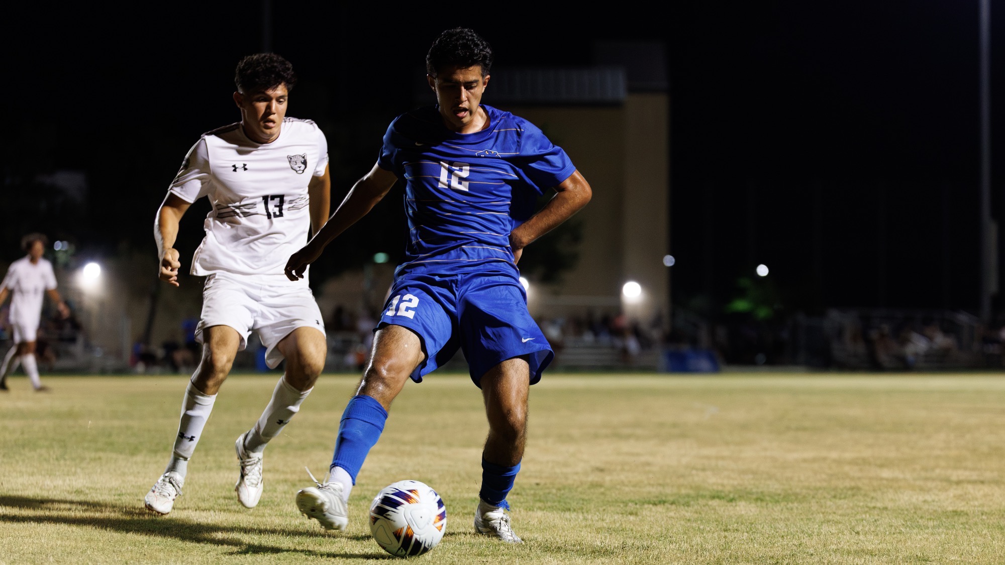 Eduardo Fernandez blocks the ball from a defender, kicking it with his right foot.