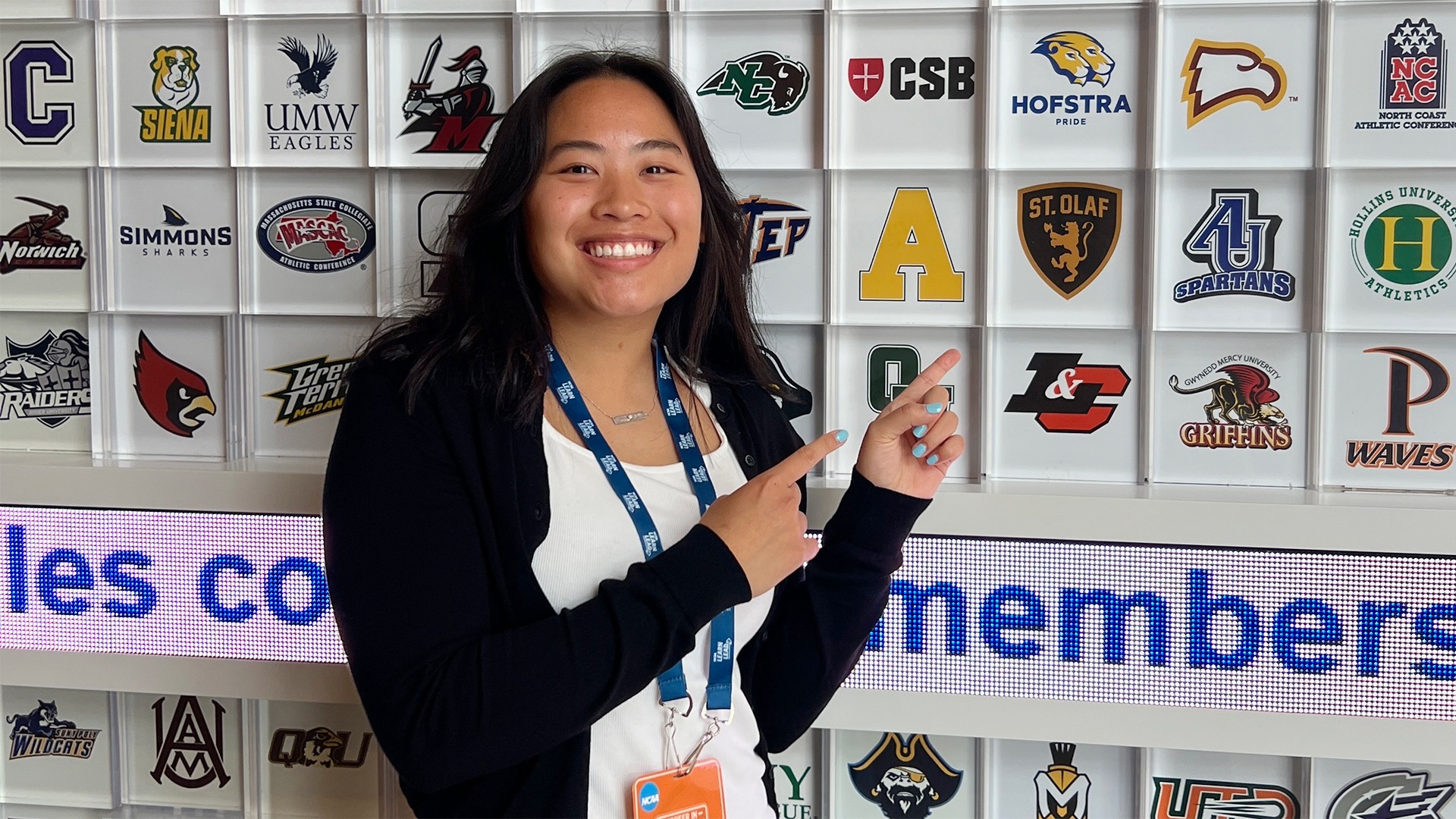 Joy Brandenstein points at the St. Olaf Athletics logo on the NCAA logo wall.