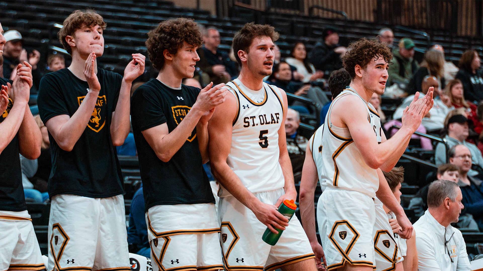 Members of the St. Olaf men's basketball team clap on the bench.